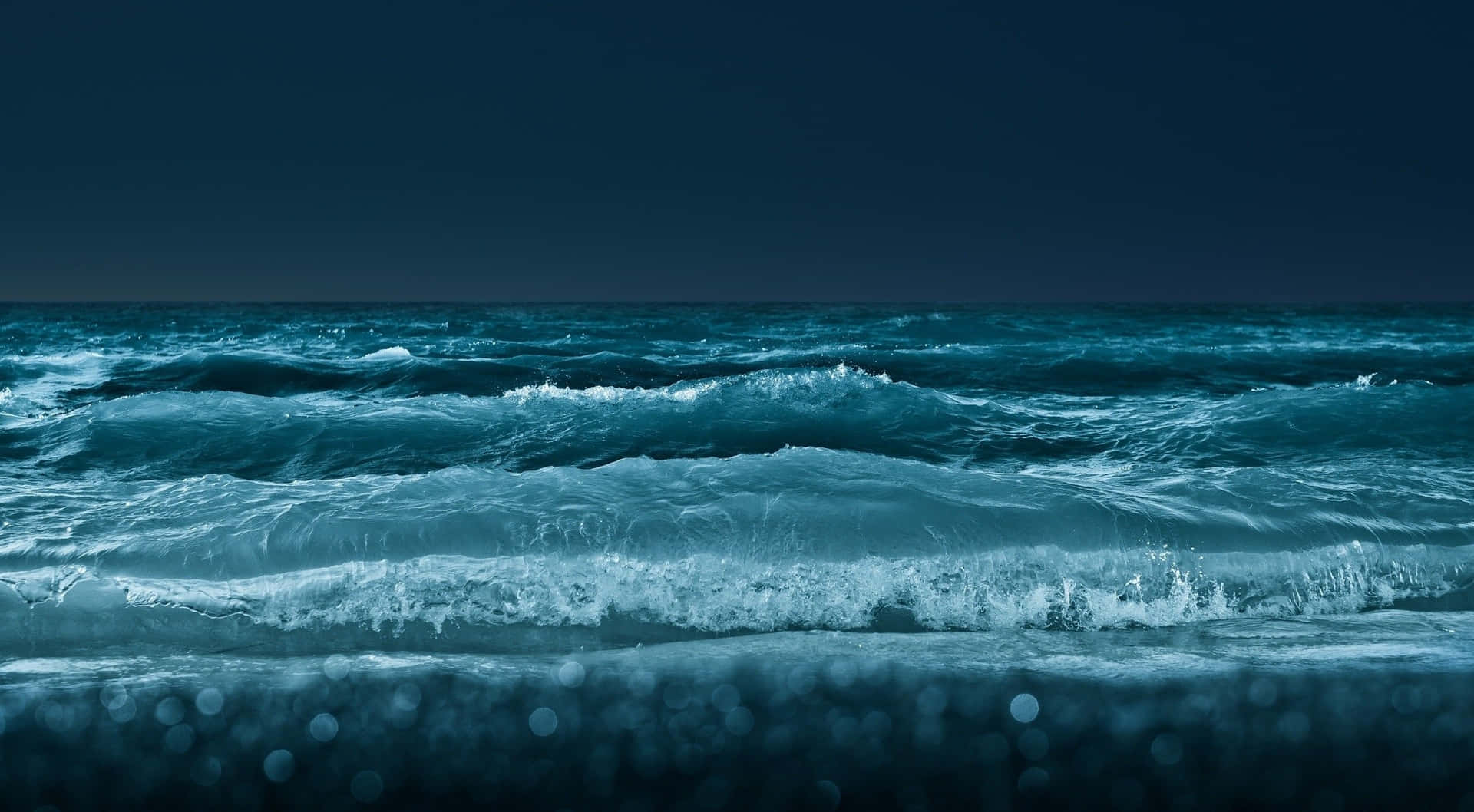 夜空下的海浪，散景燈光映照在濕沙上