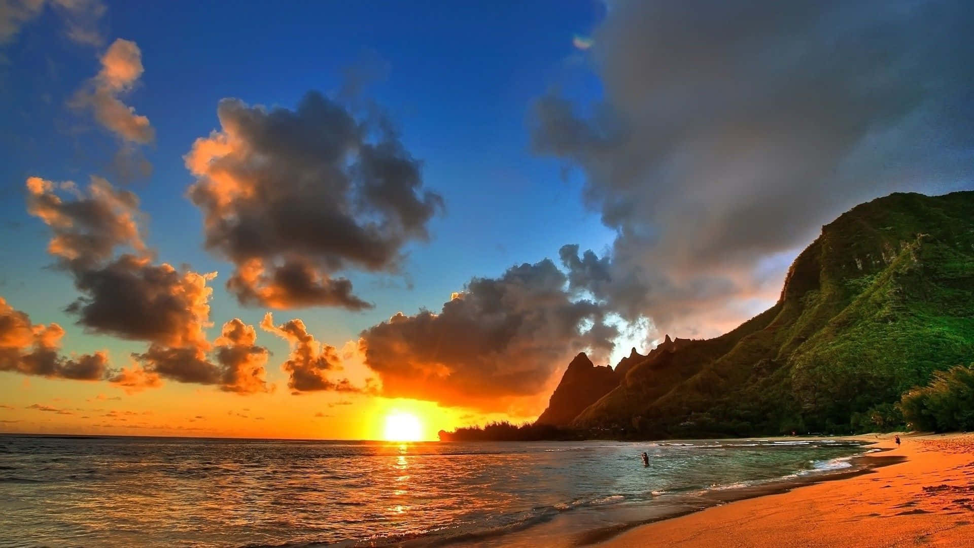 享受寧靜的海灘日落美景 壁紙 — 夕陽將天空染成橙色和藍色，海浪拍打著沙灘，旁邊是鬱鬱蔥蔥的綠色懸崖。