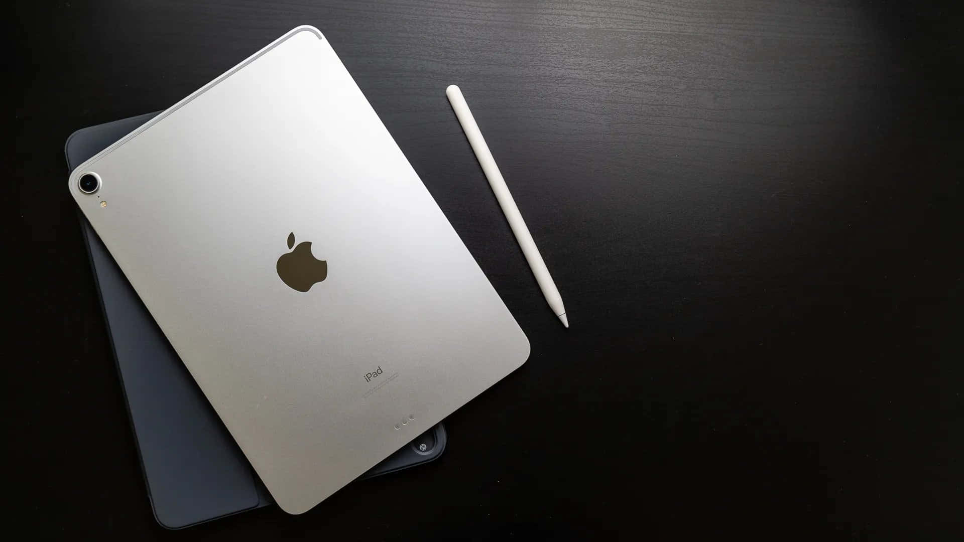 銀色iPad和白色Apple Pencil在深色木質桌面上。