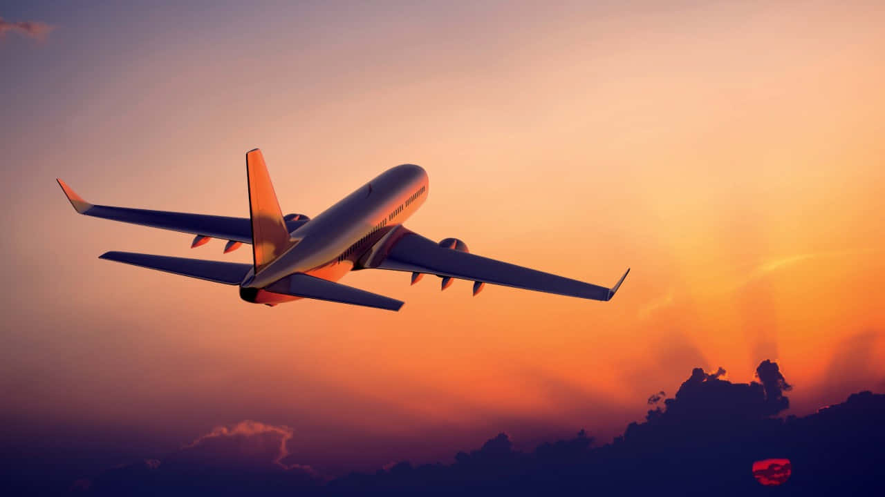 享受從天空俯瞰的寧靜景觀 壁紙 — 一架商用飛機在橙紫交織的絢麗日落天空中翱翔，下方是輪廓分明的雲層。