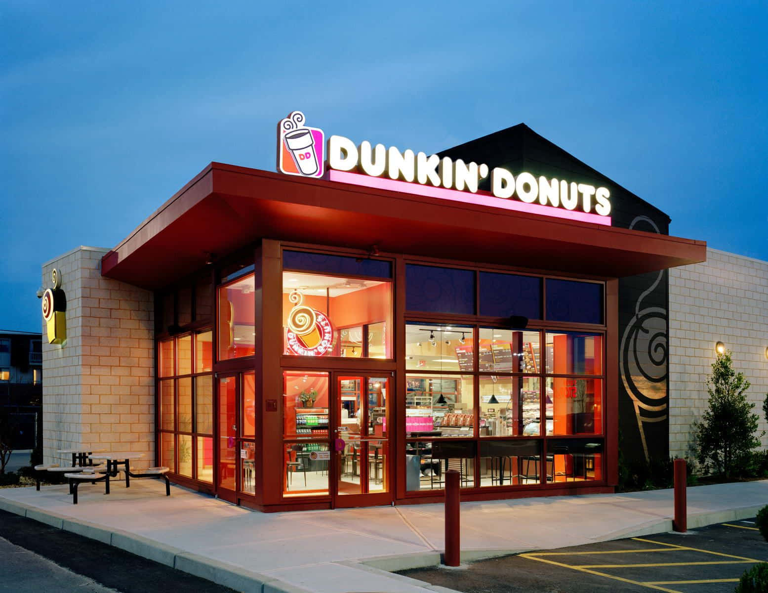 享受您最愛的Dunkin' 咖啡與甜甜圈！ 壁紙 — 黃昏時分，Dunkin' Donuts 店舖正面燈火通明，內部溫暖光線與紅色外部裝飾相映成趣。