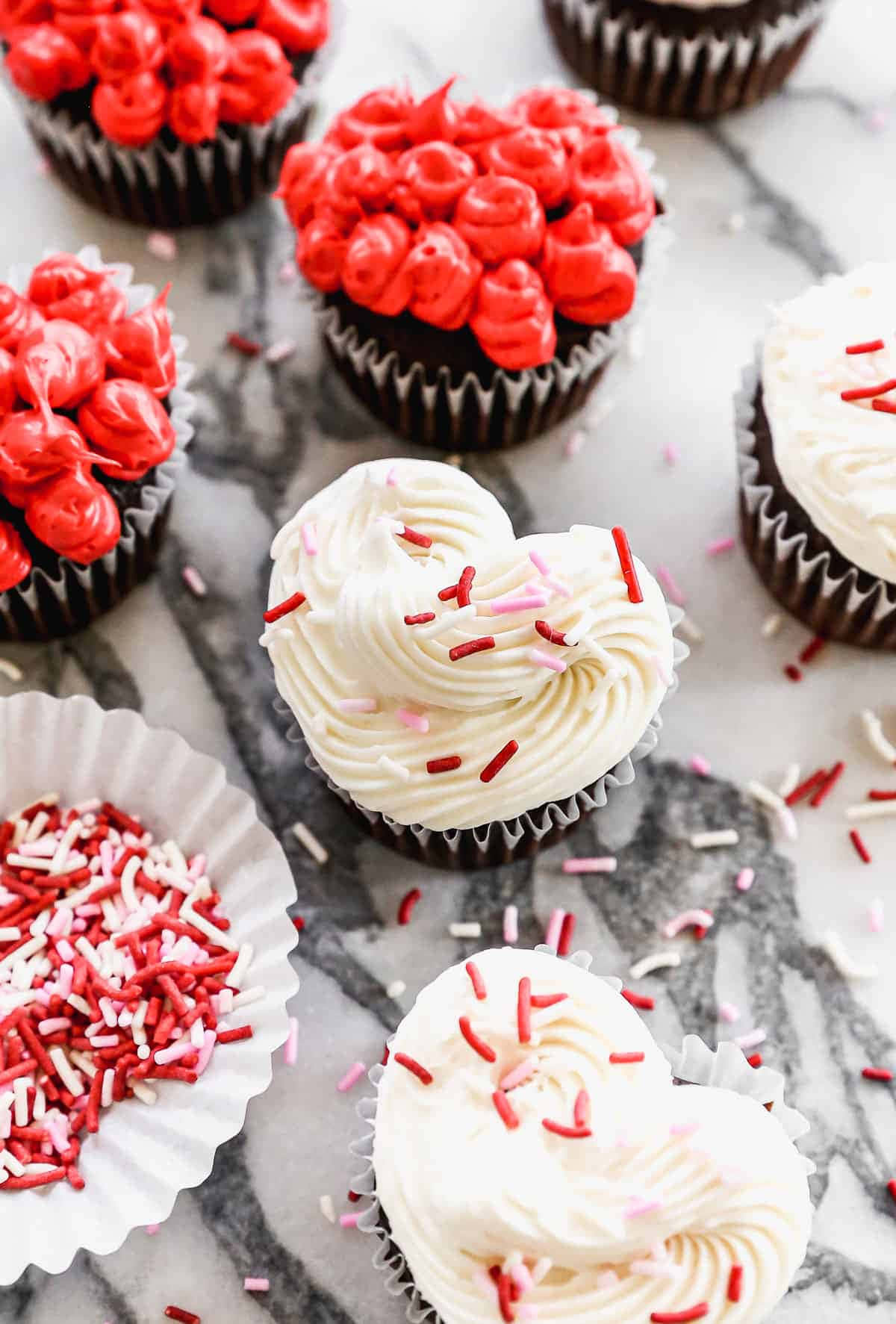 心形 cupcakes 配上紅色和白色裝飾糖粒，置於大理石檯面上。