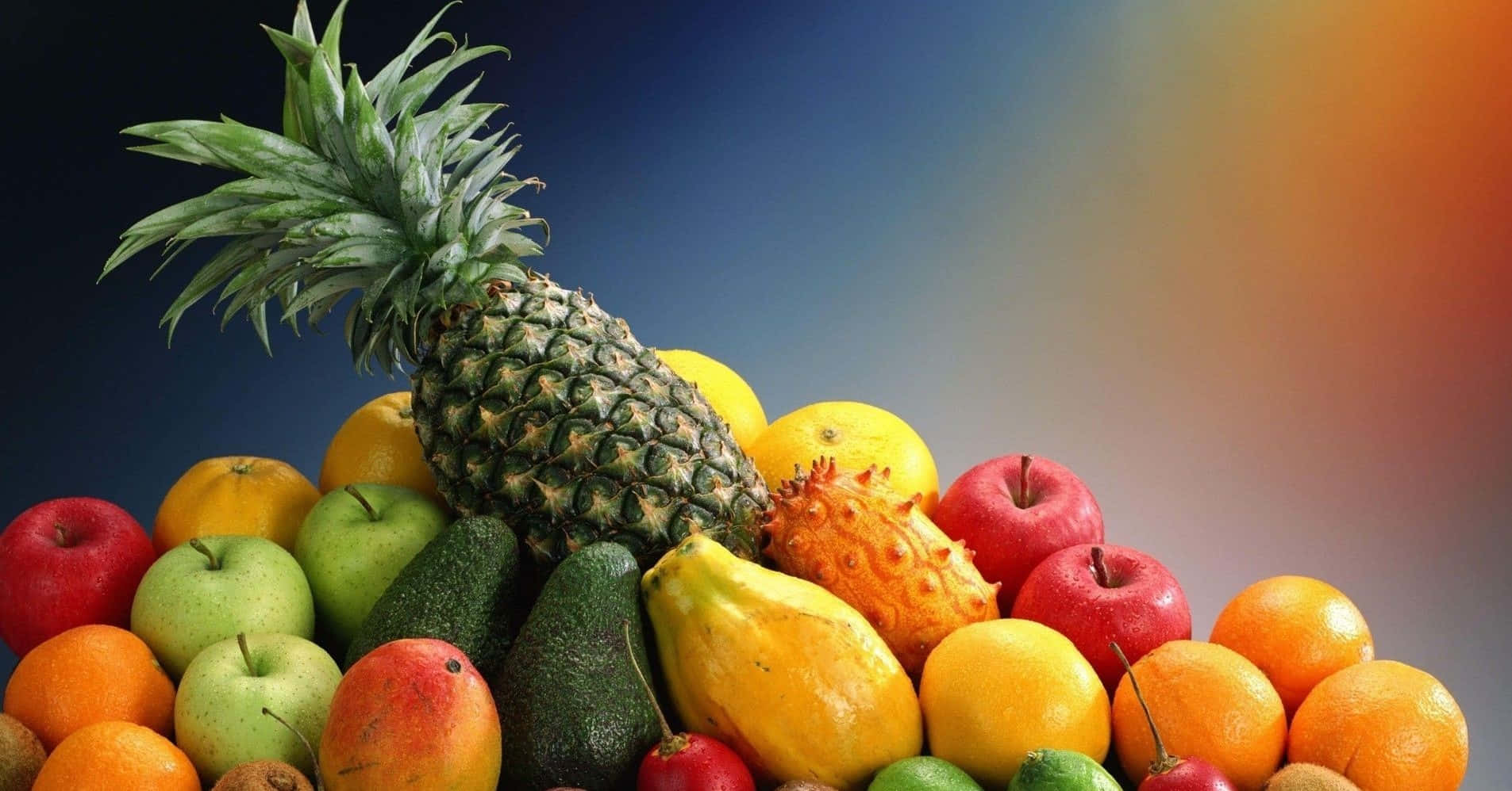 享受新鮮多汁水果的美味 壁紙 — 一堆色彩繽紛的熱帶和溫帶水果，包括菠蘿、牛油果和柑橘，背景為藍色和橙色漸變。