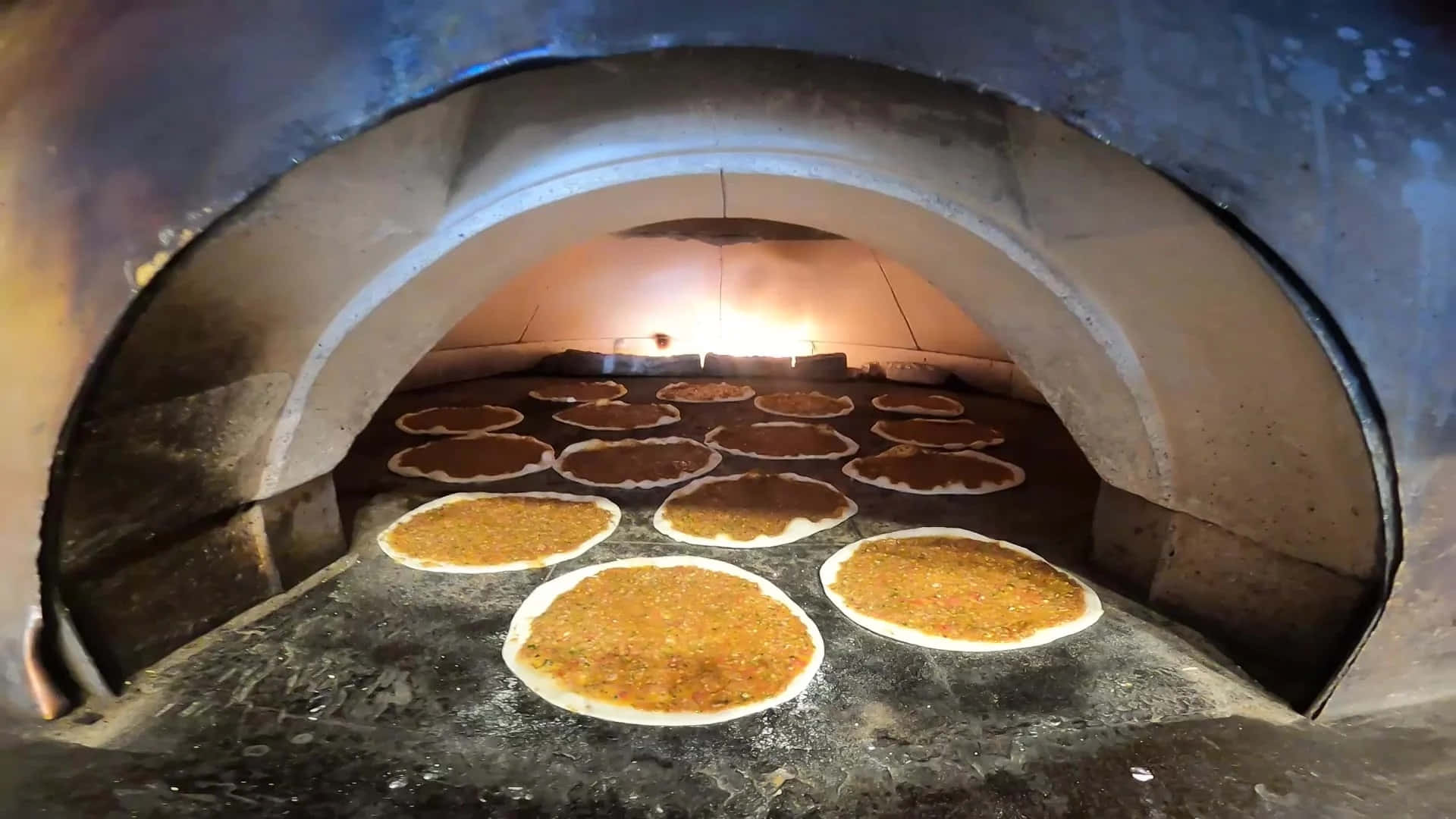 享受新鮮烘焙的美味 壁紙 — 圓形扁麵包配金色配料在發光的石窯中烘烤，帶有溫暖的環境光。