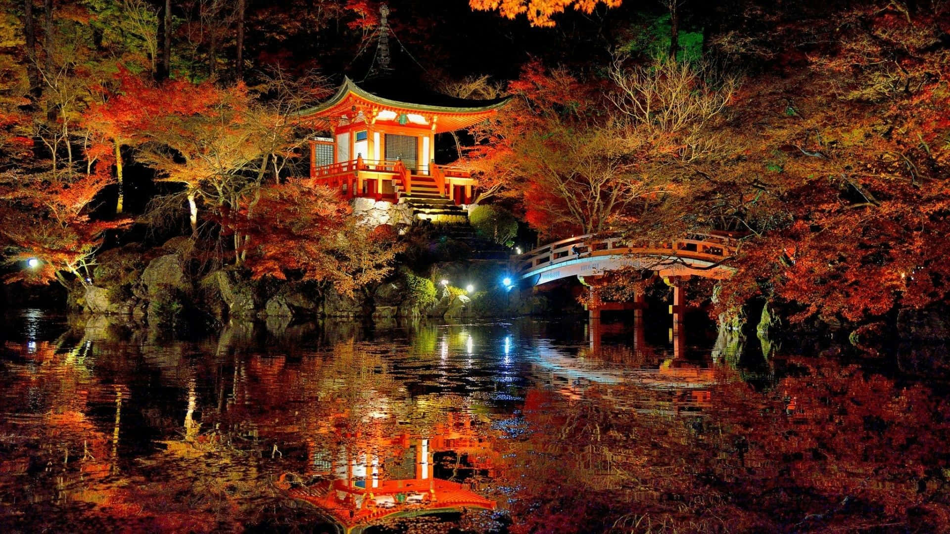 夜晚，秋樹下的水中倒映著一座明亮的日本寺廟和橋樑。
