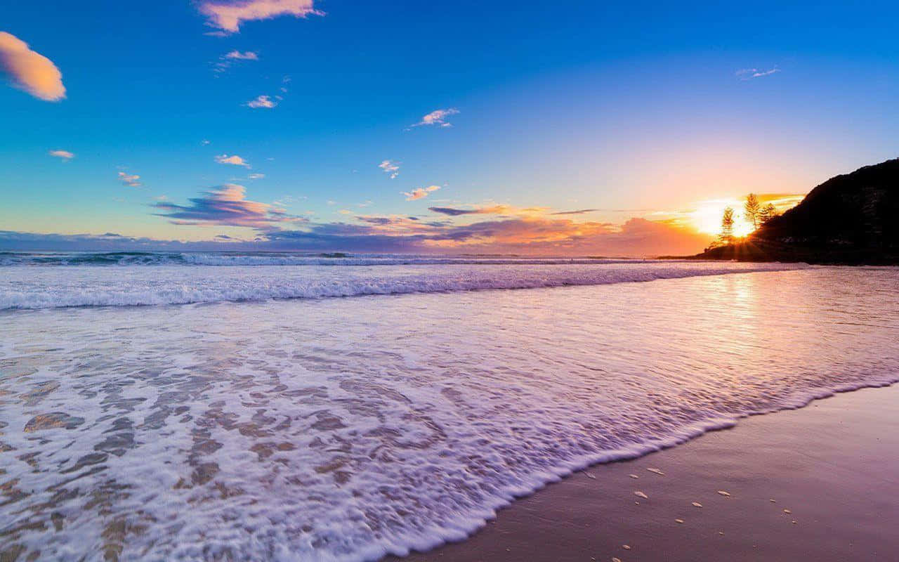 享受最棒的夏日！ 壁紙 — 夕陽將海洋染成金色，海浪在充滿活力的天空下拍打沙灘。