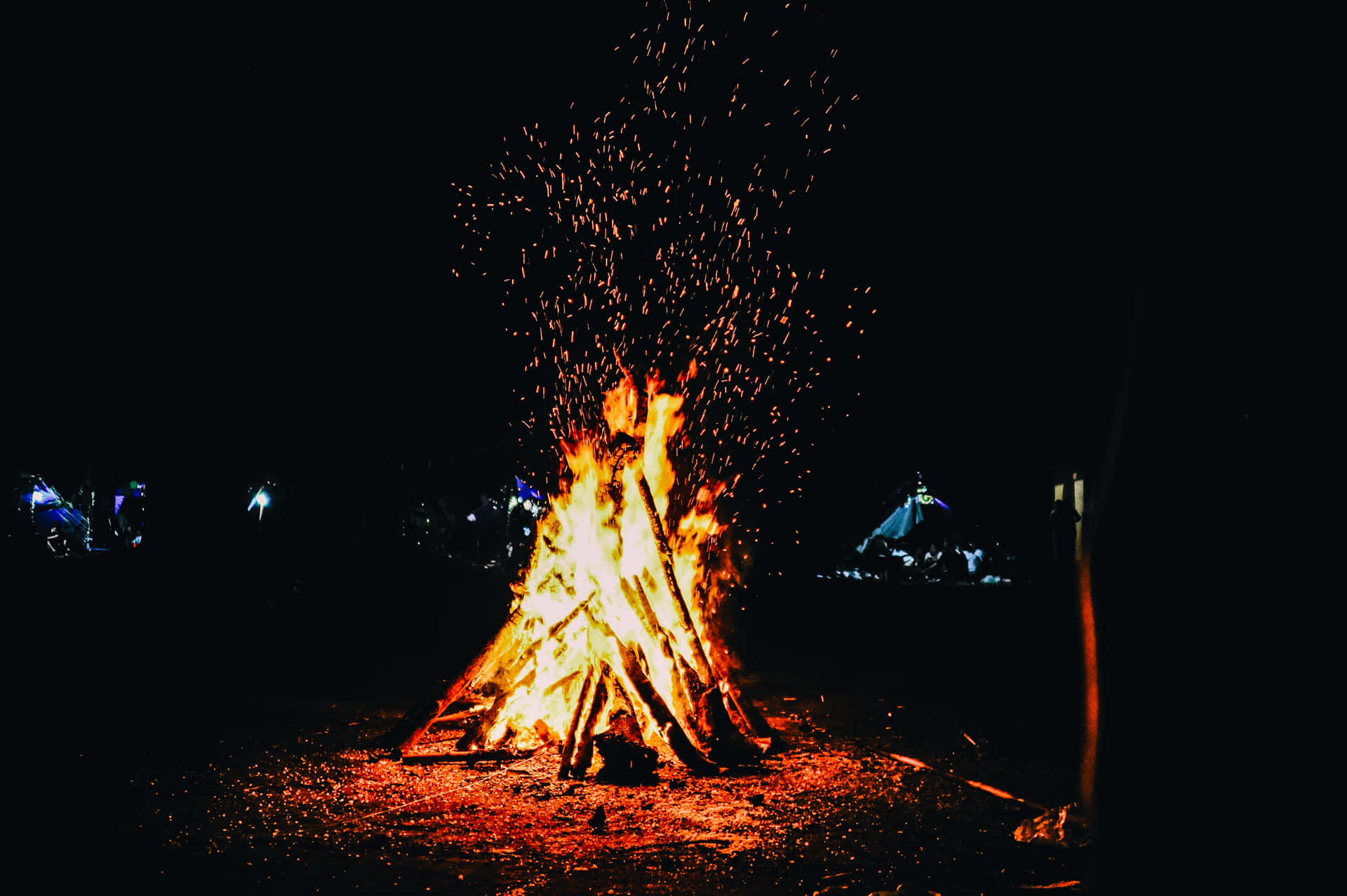 夜晚充滿活力的營火，火花四濺，背景中帳篷閃閃發光。