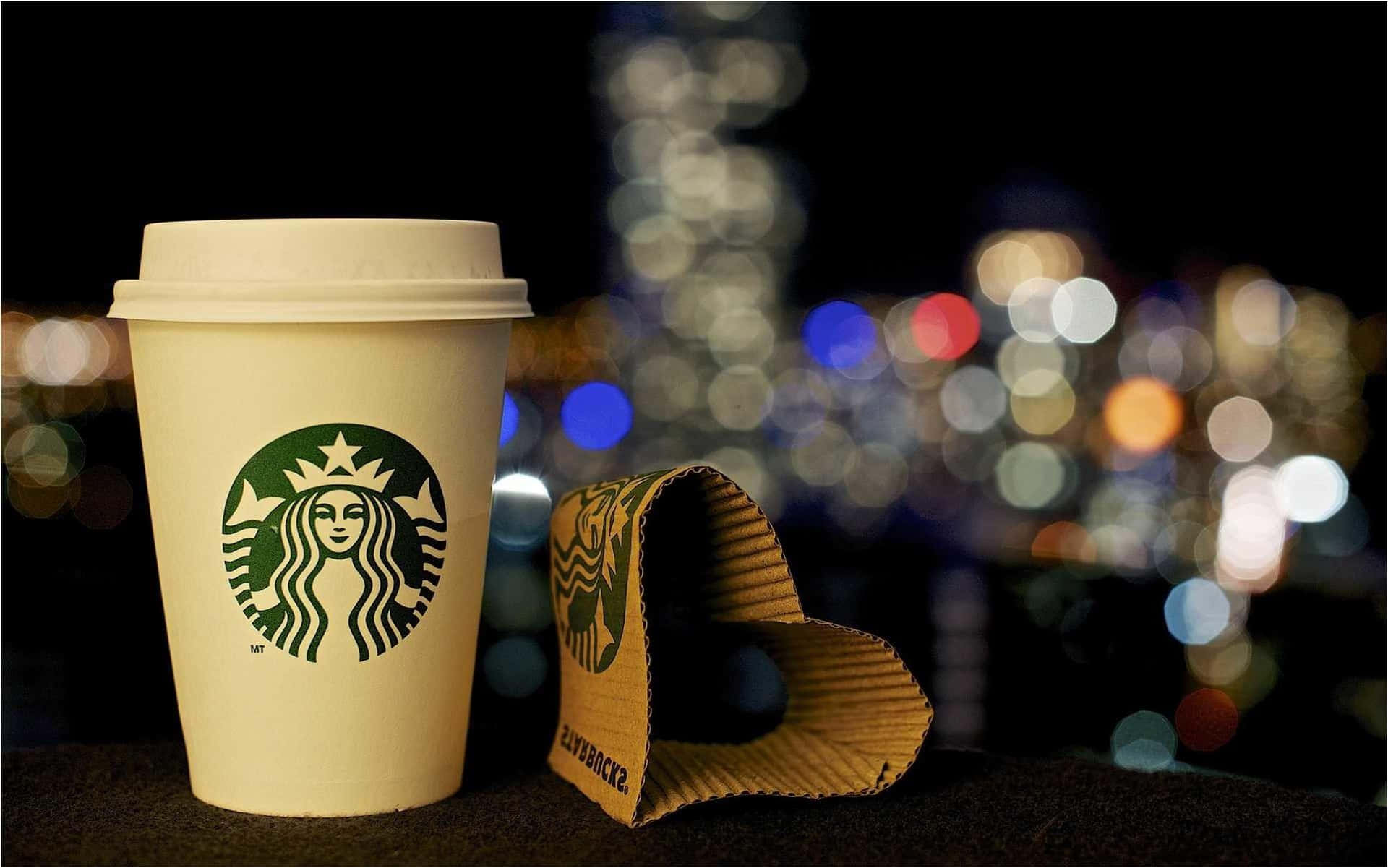 Starbucks咖啡杯和杯套在窗台上，背後是模糊的城市燈光。