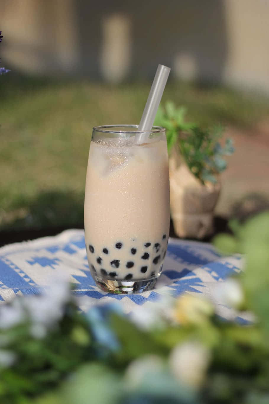 享受珍珠奶茶的氣泡與風味 壁紙 — 一杯帶有黑色珍珠的奶油泡泡茶，放在戶外藍色圖案布上的高腳杯中。
