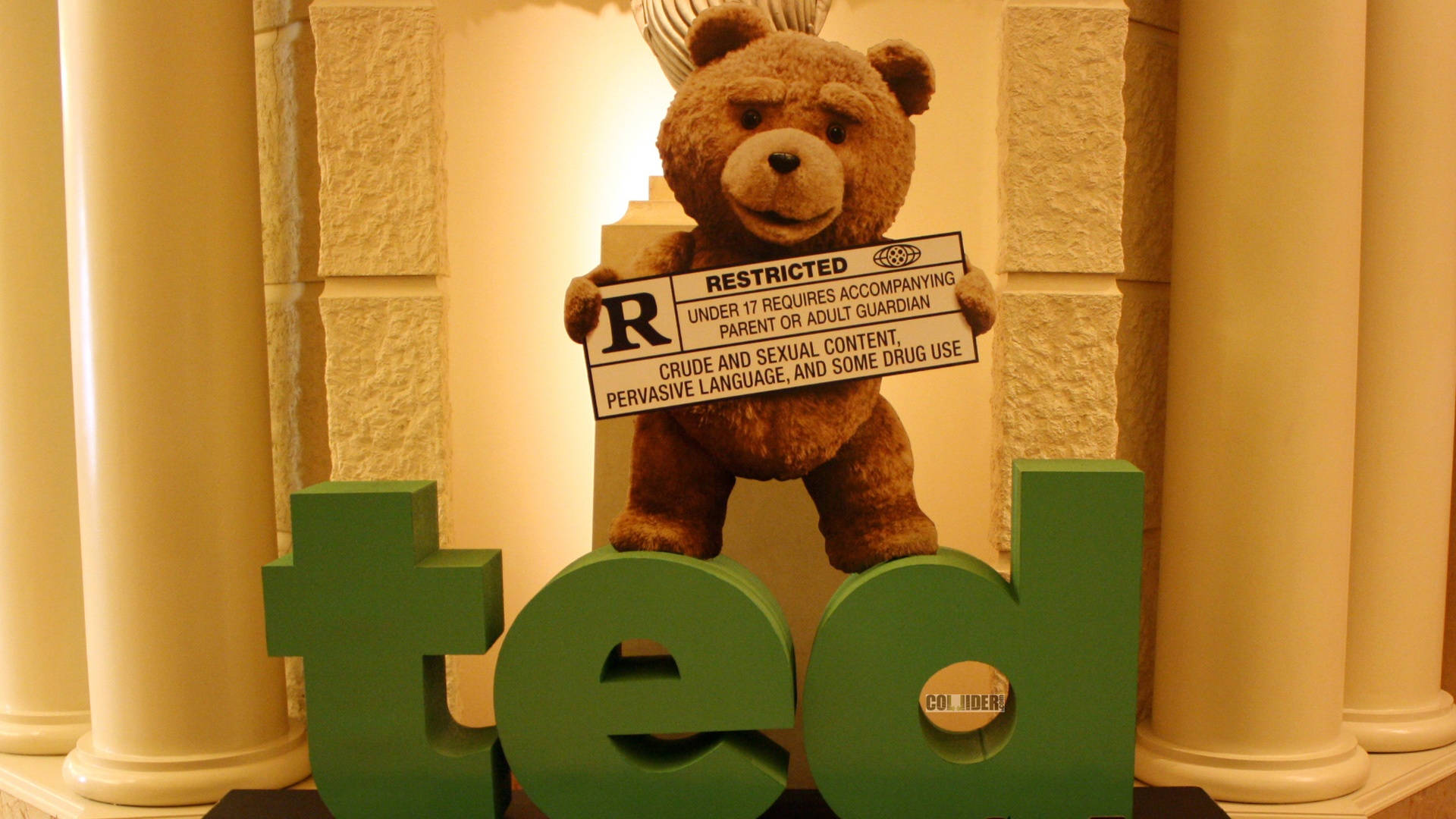 泰迪熊拿著R級電影標誌，站在石柱中綠色「ted」字母後面。
