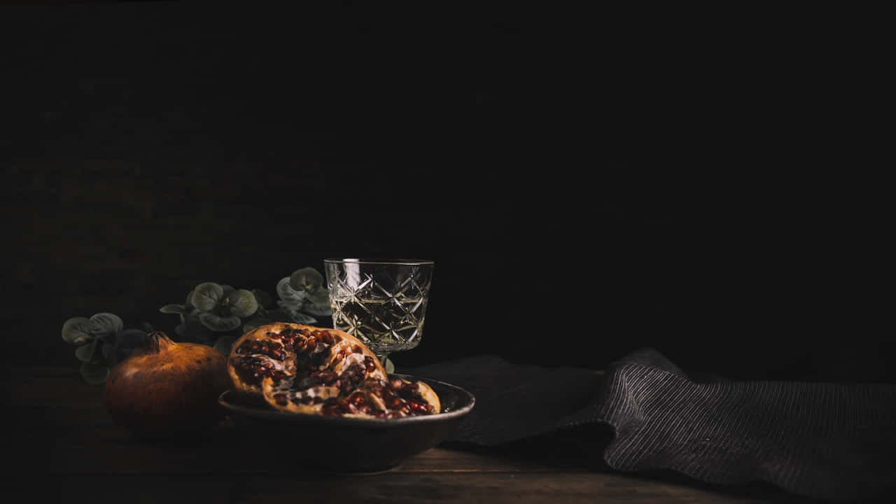 碗中的切片石榴，旁邊有完整水果和玻璃杯，置於木桌上。