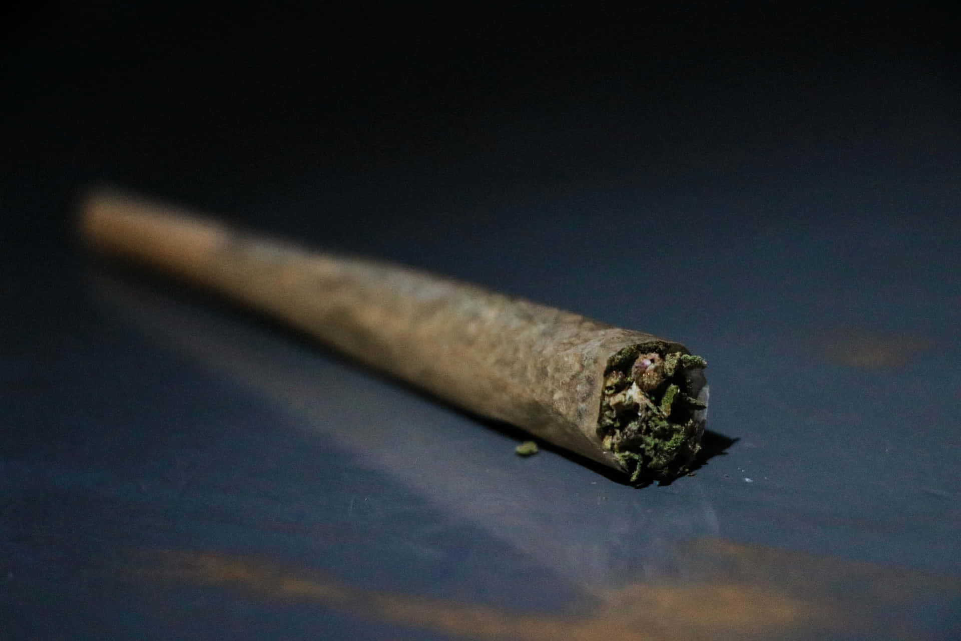 一個已點燃的大麻煙捲在深色反光表面上，煙霧裊裊升起。