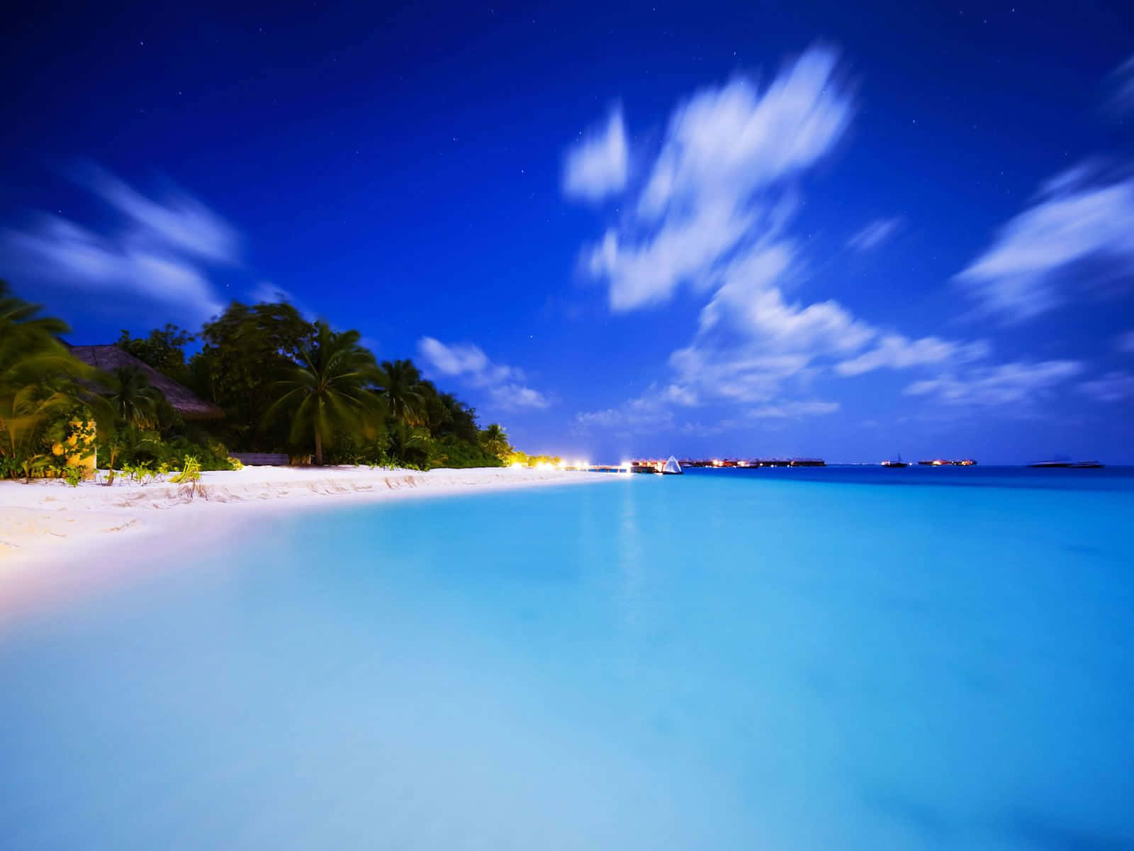 享受美麗的夏日時光！ 壁紙 — 寧靜的熱帶海灘夜景，星空流雲，碧綠海水，沿岸度假村燈光閃爍。