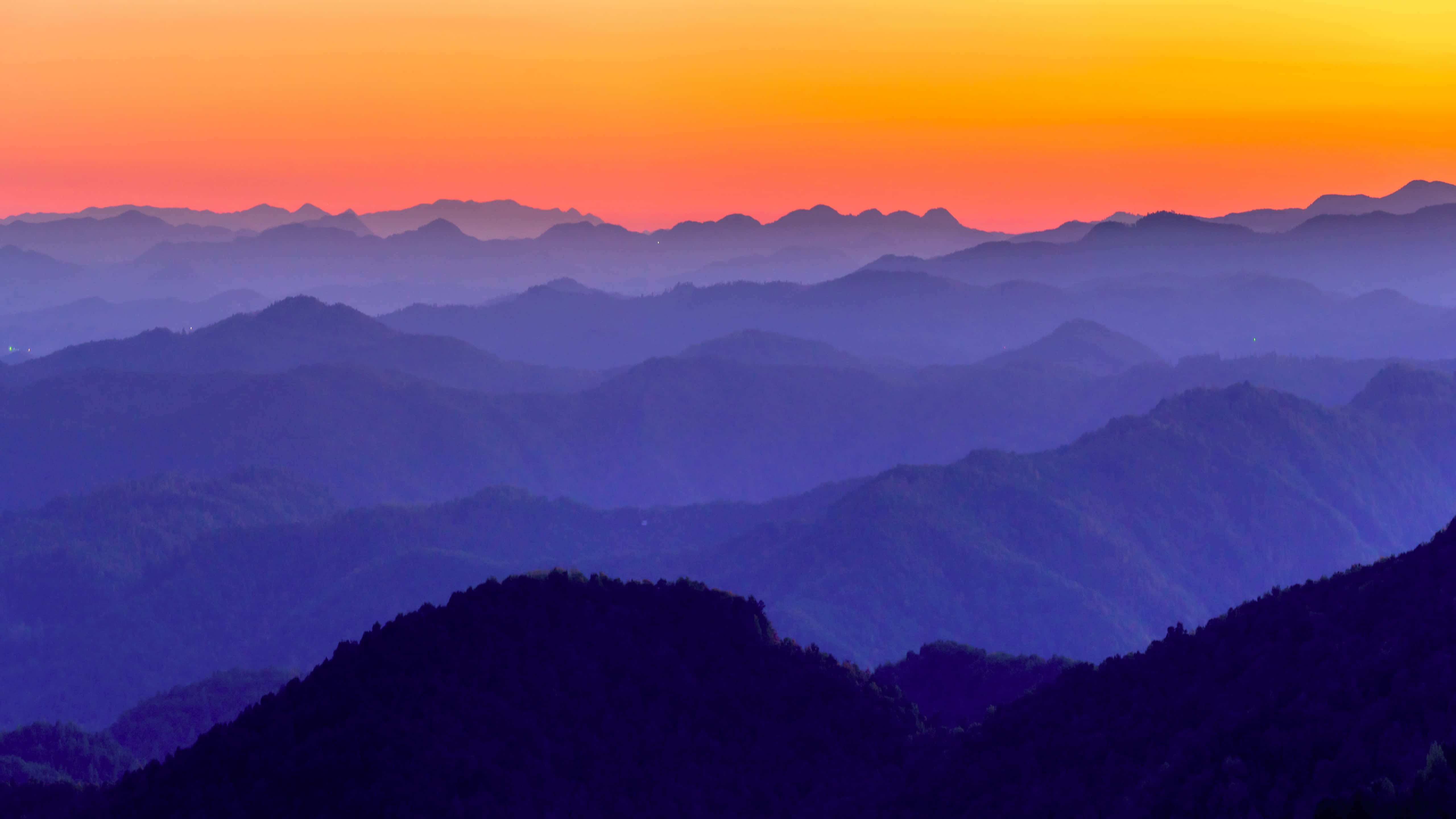 在鮮豔橙紫夕陽天空下的霧氣山脈。