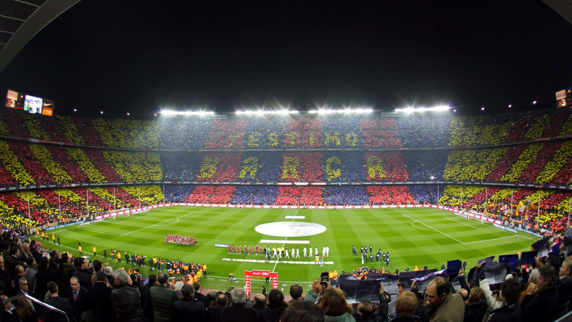 夜間足球場，球迷舉起紅、黃、藍色橫幅拼出 BARÇA。