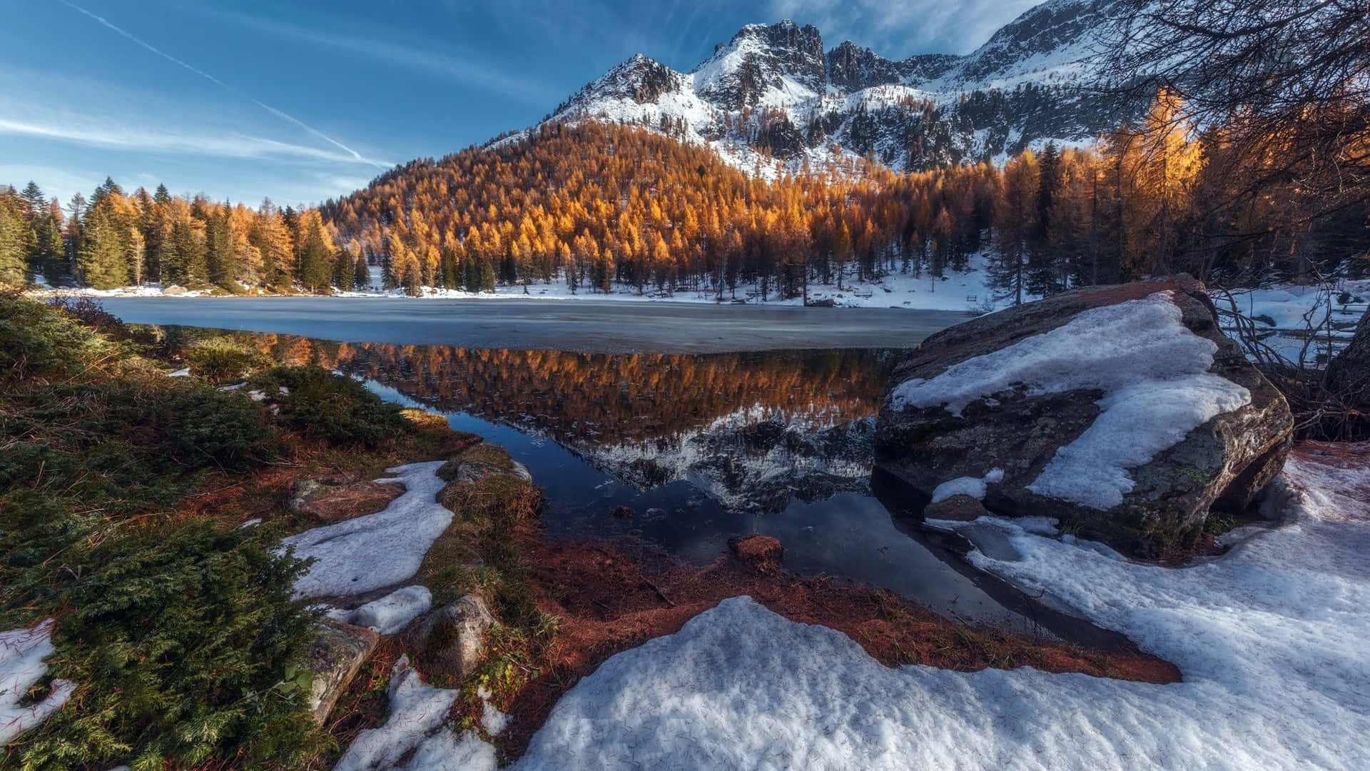 享受雄偉的山景 壁紙 — 冰封的山湖映照著白雪覆蓋的山峰和金色秋樹，在清澈的藍天下。