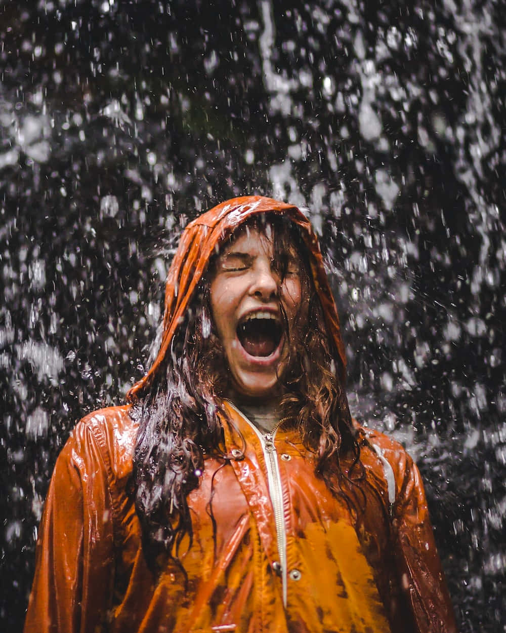 穿著橙色雨衣嘅人喺大雨中閉眼大笑。