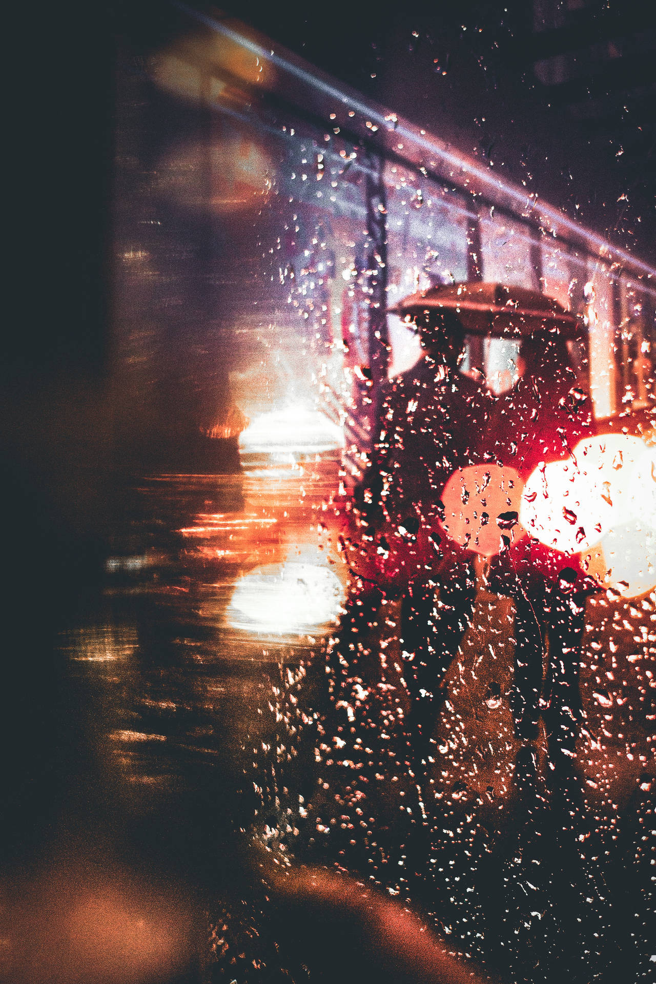 撐傘的人在雨夜城市中穿過模糊燈光行走。