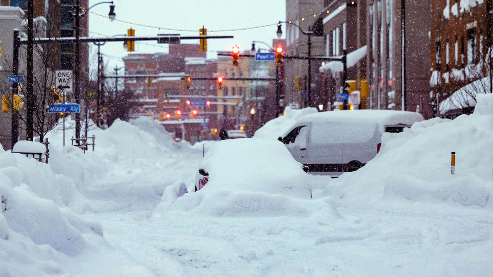 享受雪景與冬日魔幻氛圍 壁紙 — 白雪覆蓋城市街道，汽車被埋在雪堆下，交通燈在冬季風暴中發出紅光。