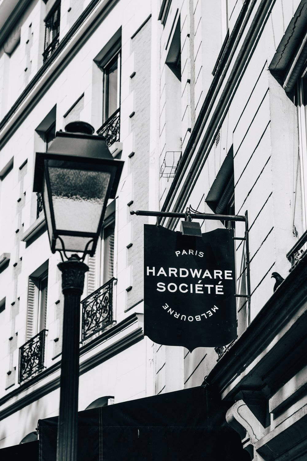 黑白街景，歐洲建築上有復古燈和Hardware Société標誌。
