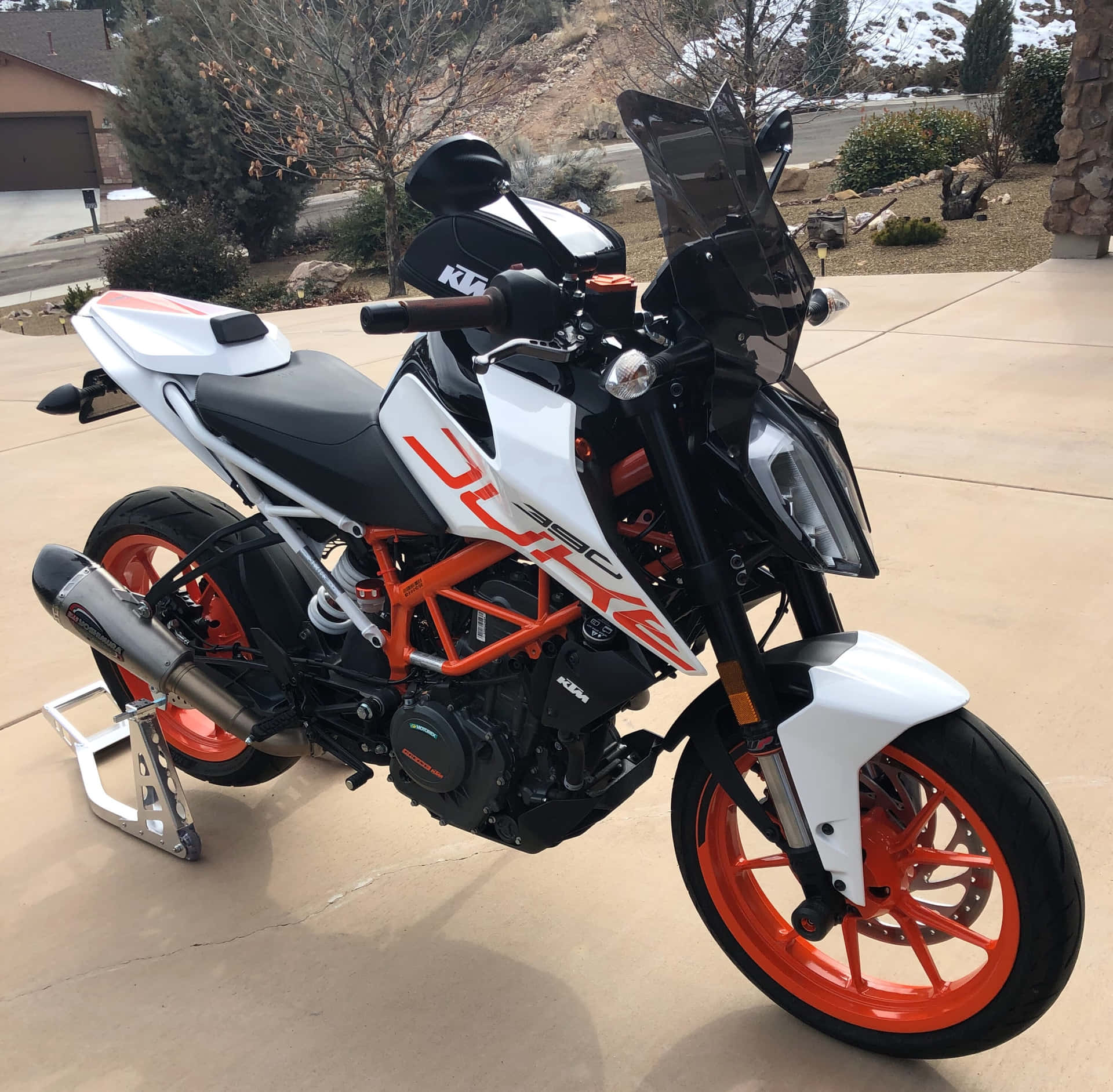 白色和橙色的KTM Duke 390電單車停放在車道上，後面有白雪覆蓋的山脈。