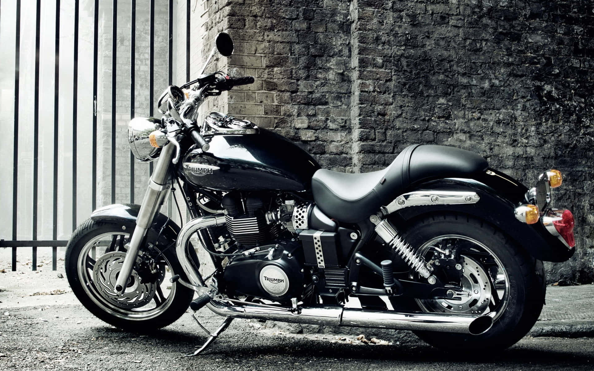 黑色 Triumph 電單車停泊喺磚牆旁邊，帶有金屬圍欄