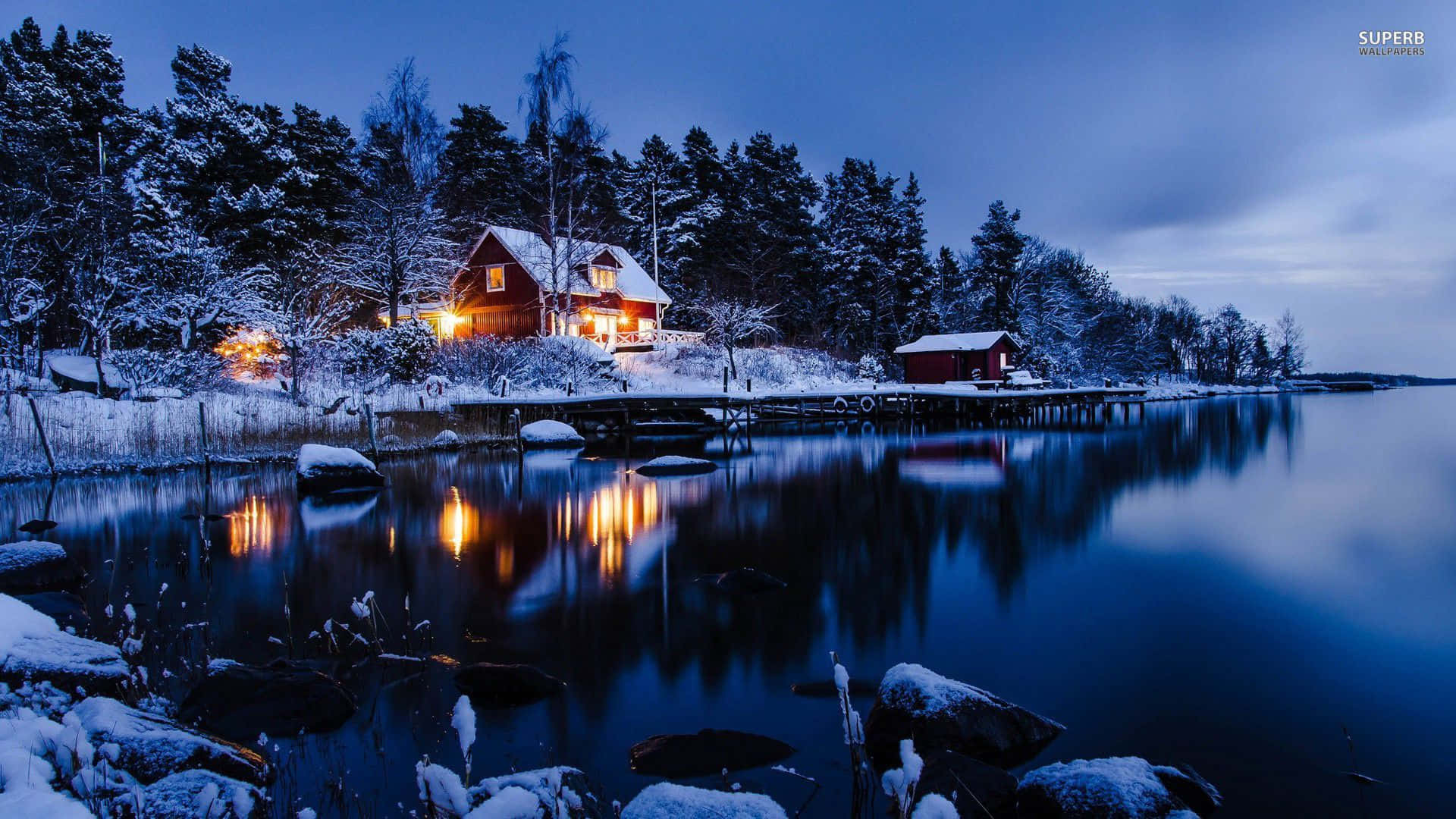 享受高清雪景之美 壁紙 — 一間舒適的紅色小屋，溫暖的燈光在暮色天空下的雪湖岸邊閃耀。