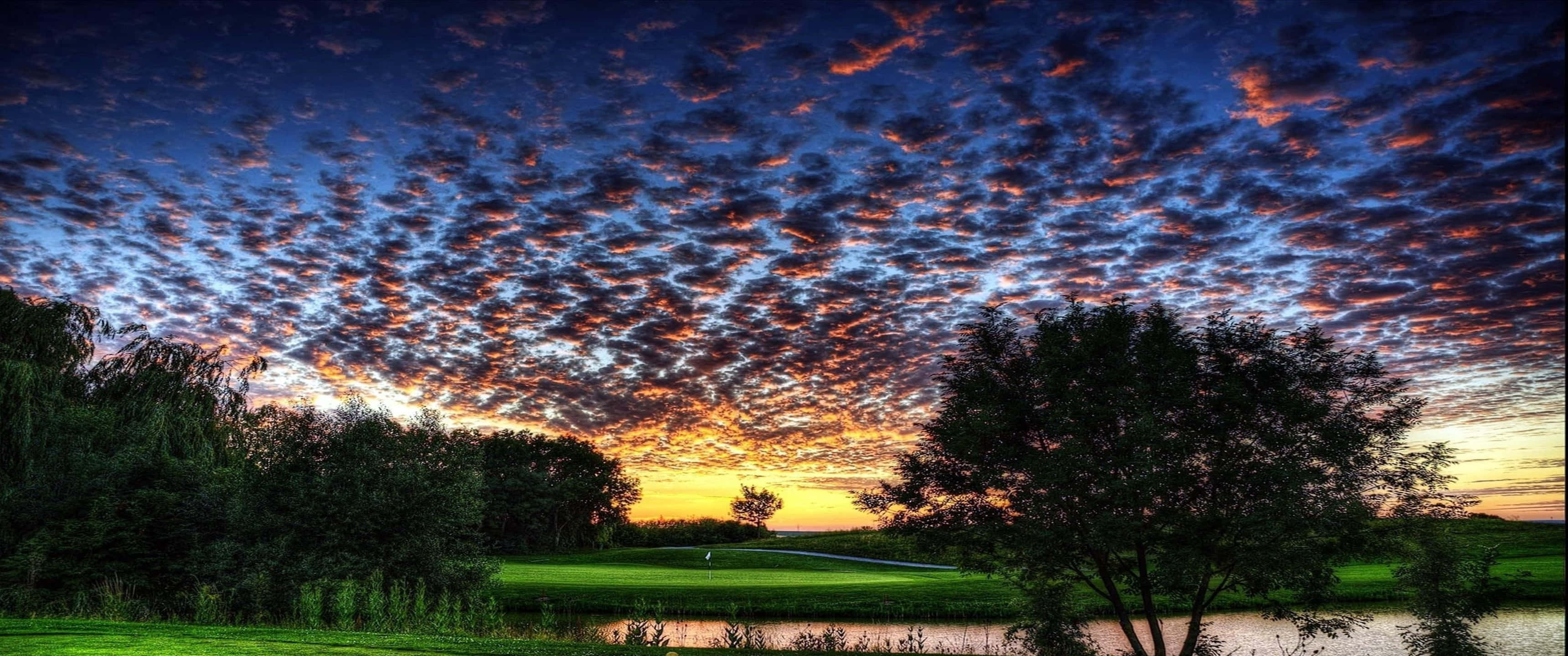 享受高爾夫球場的美景與寧靜 壁紙 — 夕陽西下，天空被染成火熱的橙色和深藍色，映襯著寧靜的高爾夫球場，樹木剪影環繞。