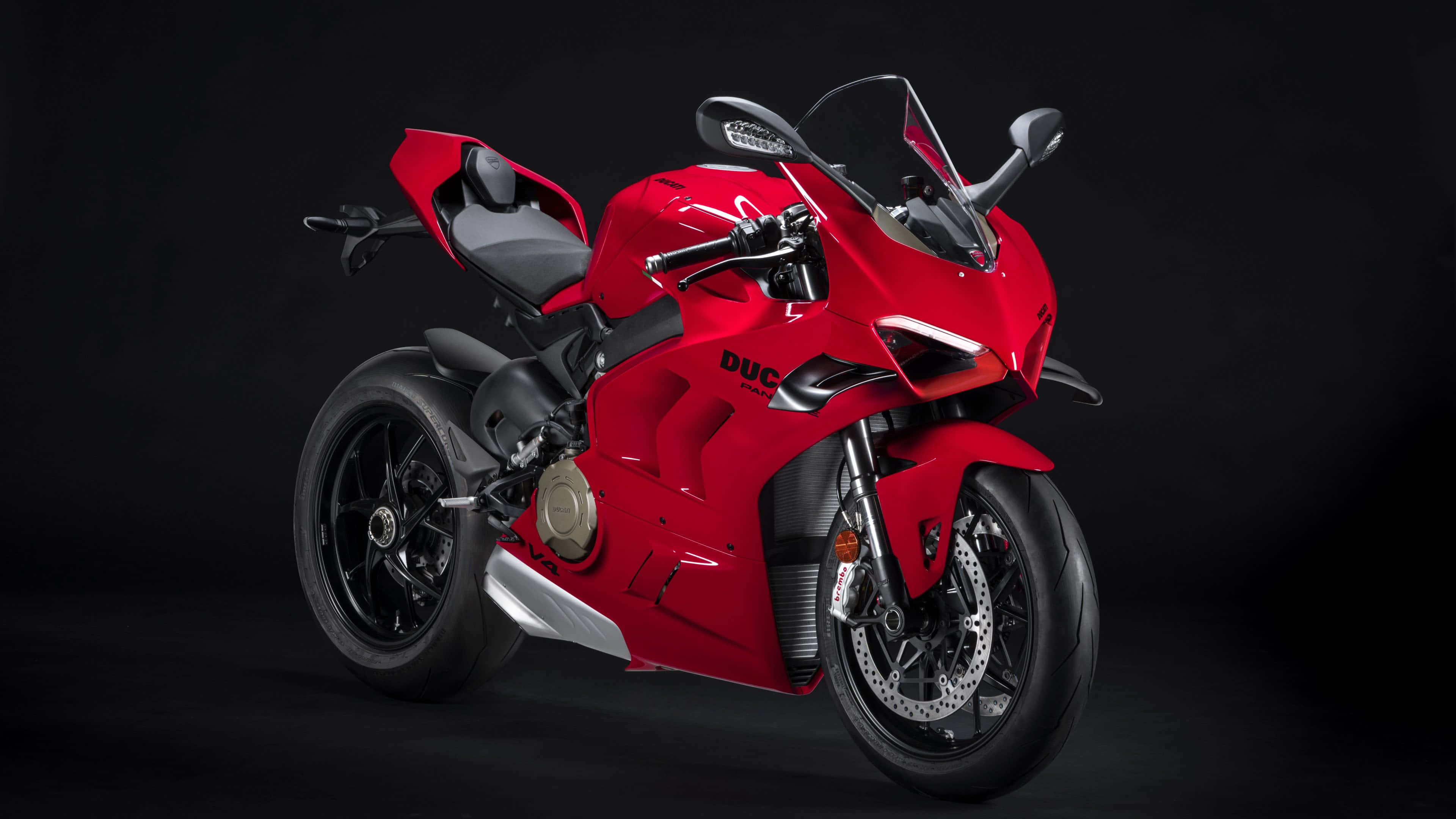 享受高速刺激的自行車騎行樂趣 壁紙 — 一輛時尚的紅色Ducati電單車，帶有黑色點綴和銀色排氣管，在深色工作室背景前蓄勢待發。