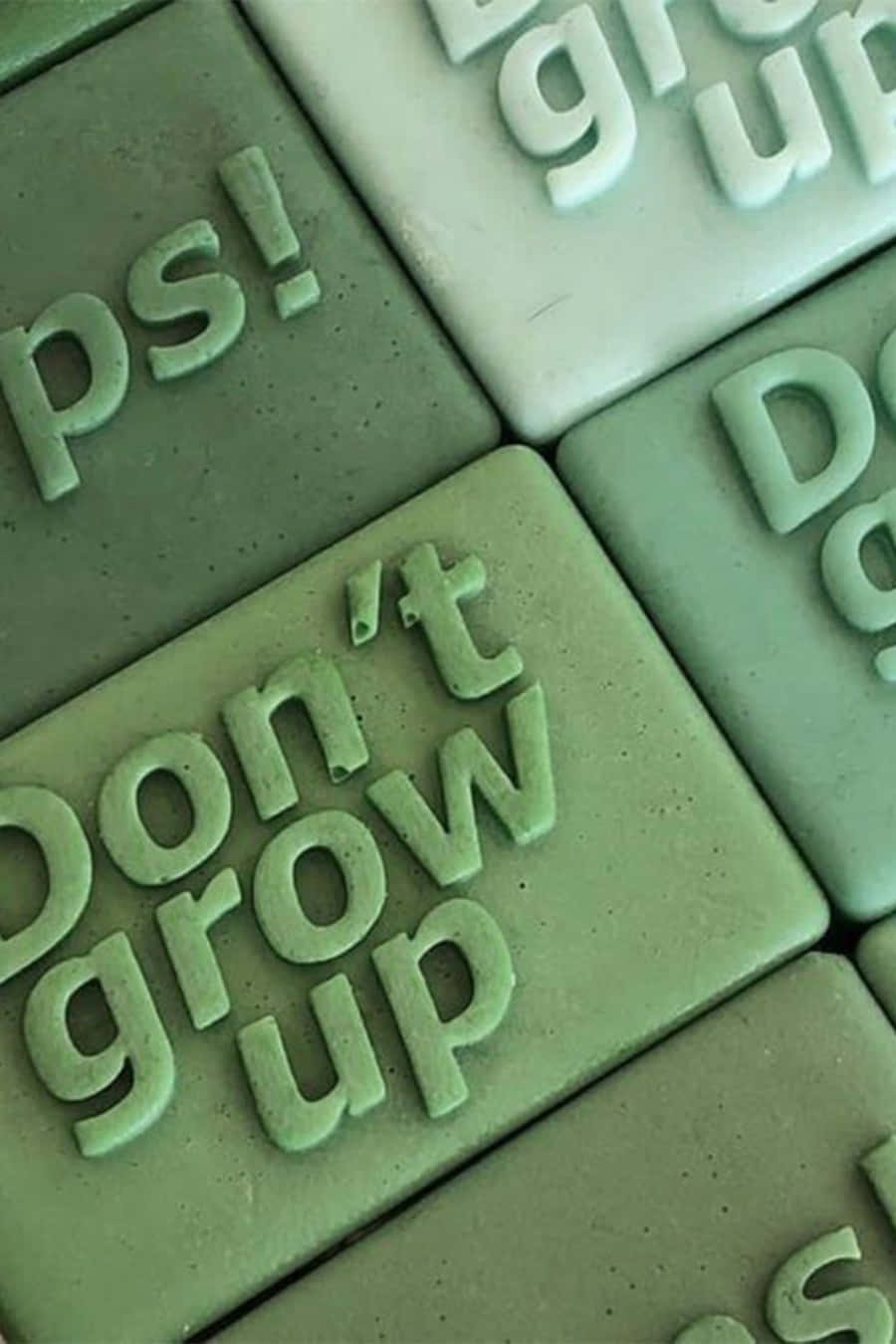 綠色瓷磚，上面有凸起的文字「Don't grow up」和「grows up」。