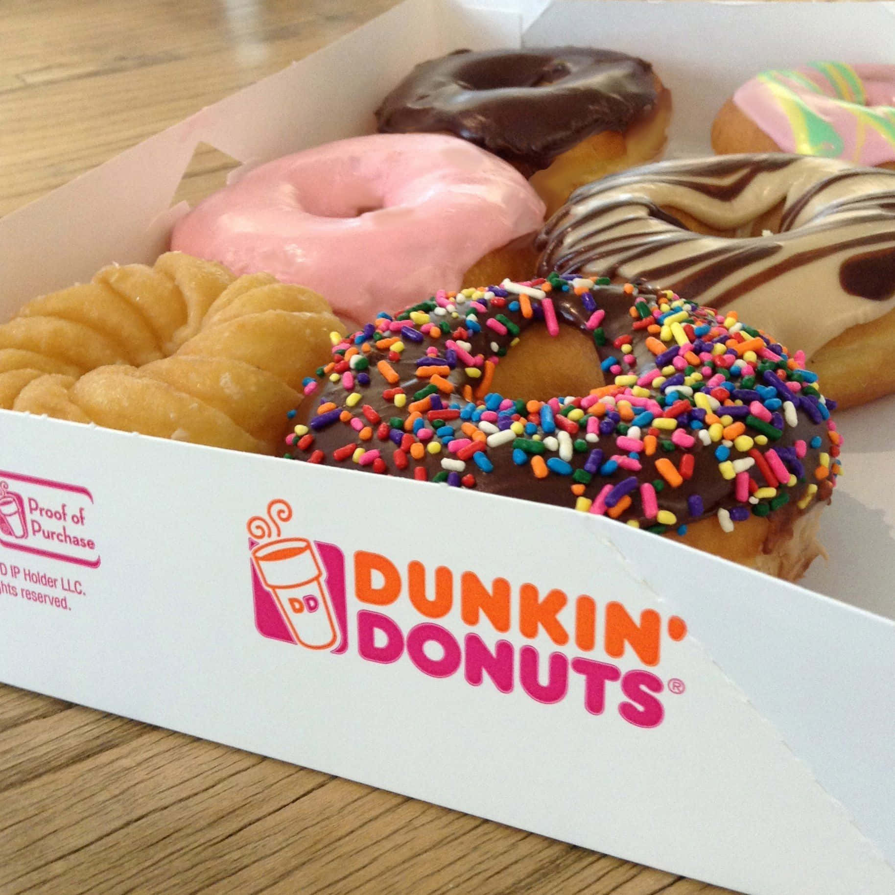 一盒各種Dunkin' Donuts，在木質表面上配有色彩繽紛的配料。