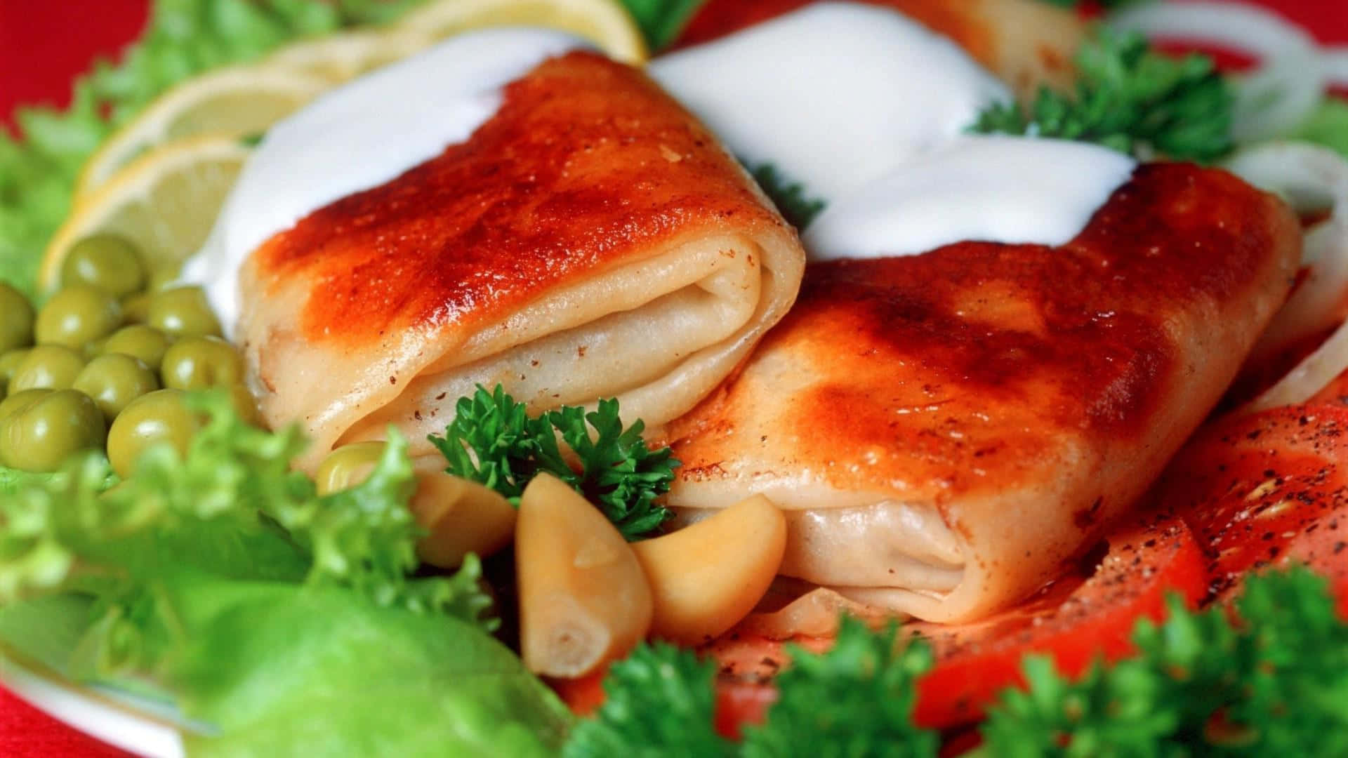 享用新鮮海鮮大餐 壁紙 — 金黃色嘅魚柳卷，上面淋上忌廉醬汁，用新鮮番茜、檸檬片同青豆裝飾，放喺鮮紅色嘅碟上。