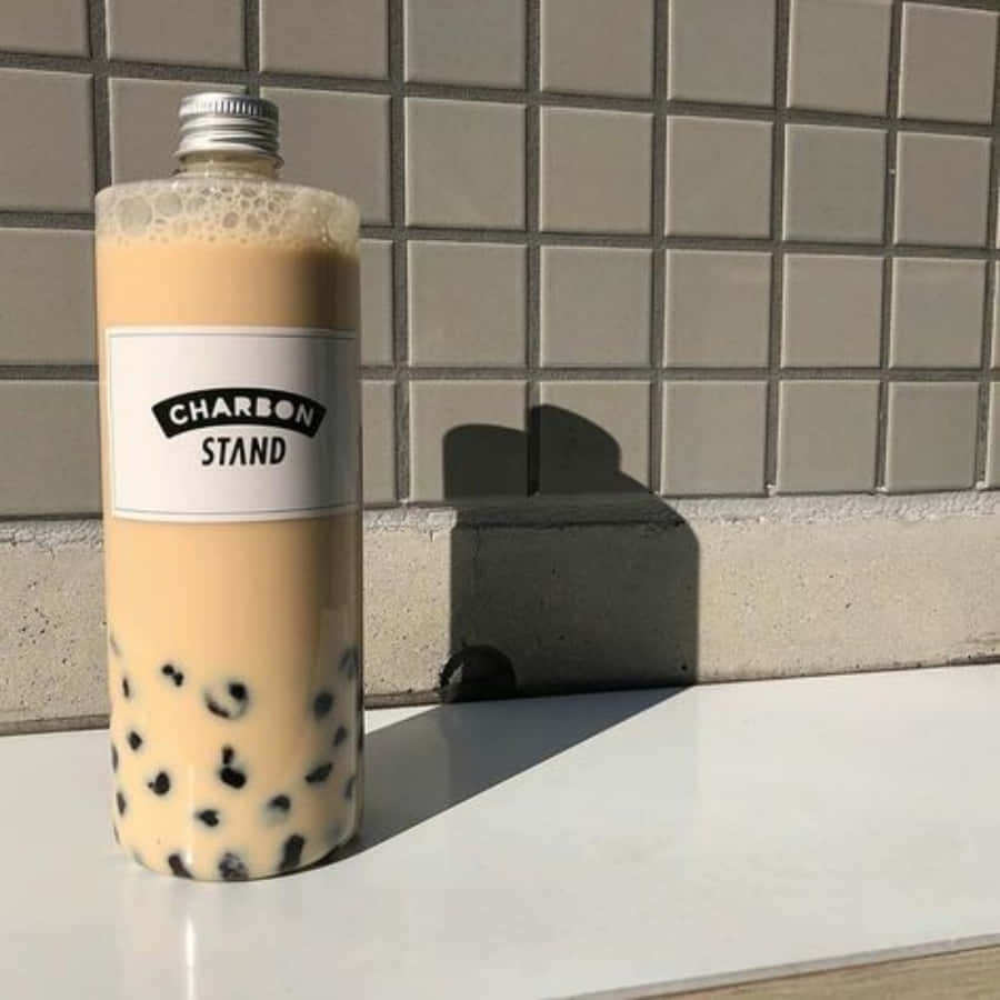 享用風味獨特的珍珠奶茶，搭配Q彈果凍球！ 壁紙 — 一個高身嘅珍珠奶茶樽，裡面有黑色珍珠，擺喺白色表面上，對住磁磚牆，喺明亮陽光下。