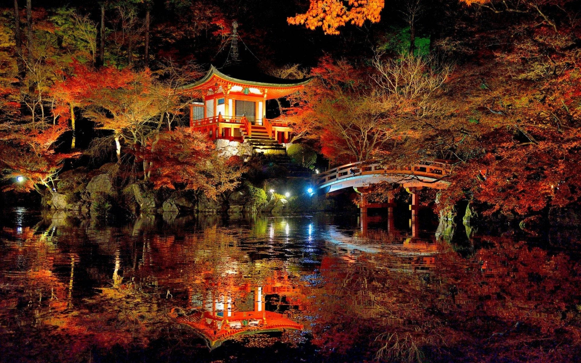 京都夜間秋季的醍醐寺 壁紙 — 夜晚，在火紅秋樹下，一座發光的紅色日本寺廟和拱橋倒映在平靜的水面上。