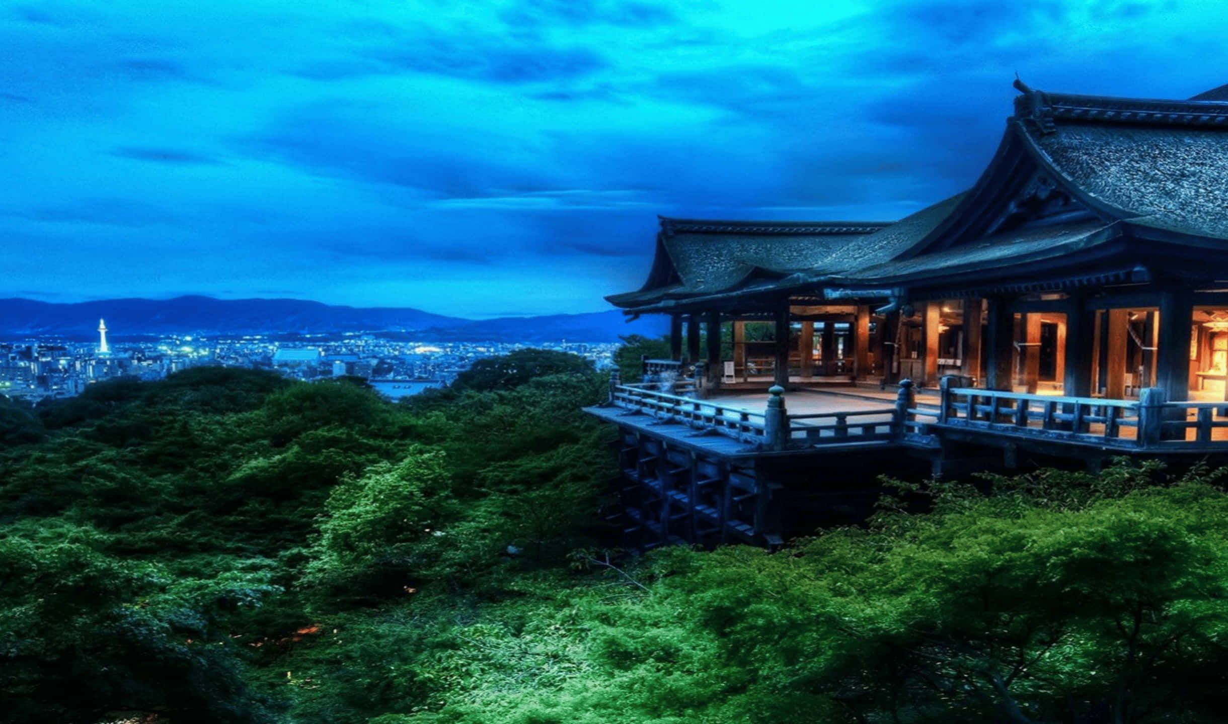 京都清水寺 2440x1440 監視器背景 壁紙 — 一座傳統木造寺廟坐落在鬱鬱蔥蔥的山丘上，俯瞰著深藍色暮色天空下的廣闊城市景觀。