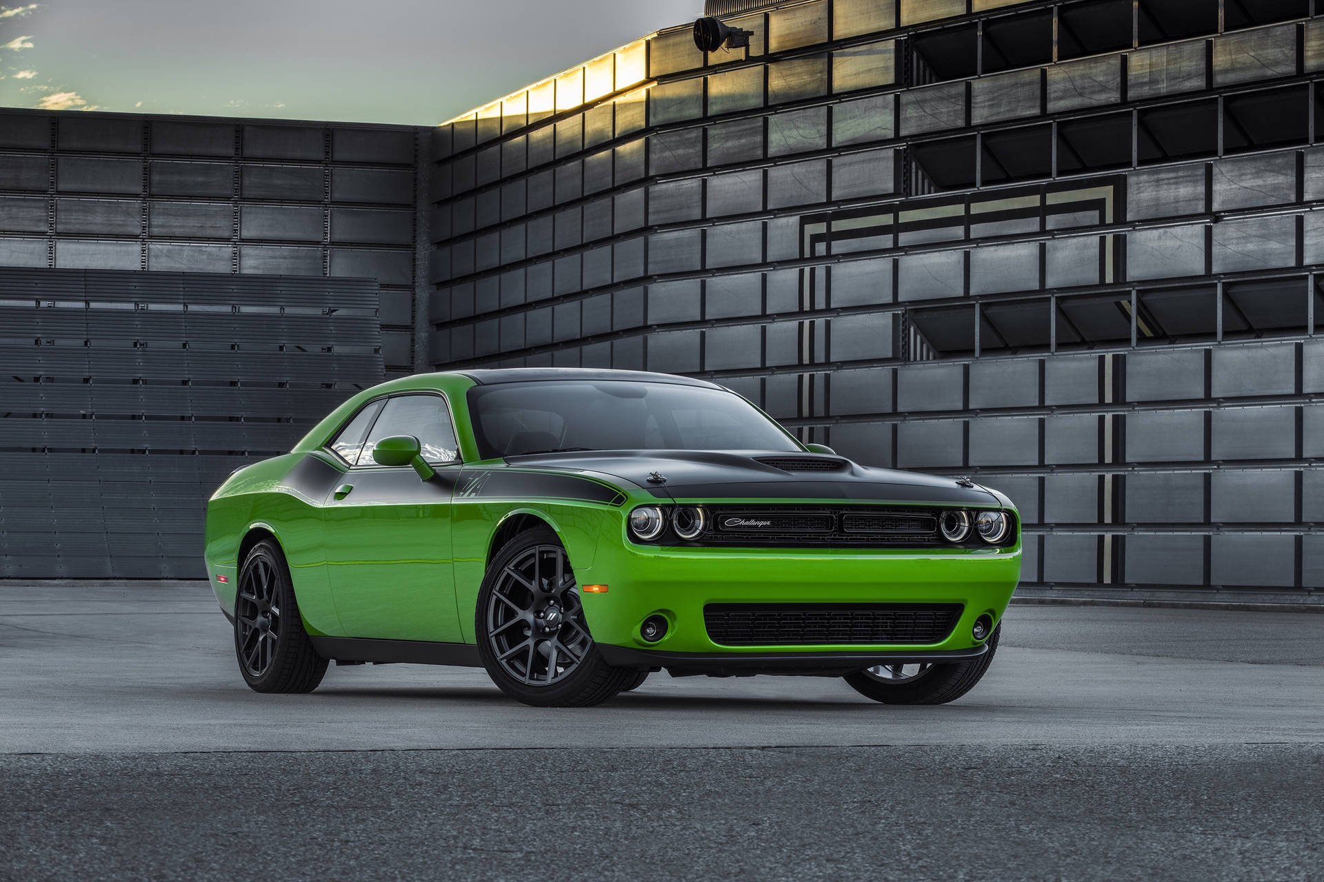 充滿活力的綠色Dodge Challenger在黃昏時停在一座現代金屬建築前。