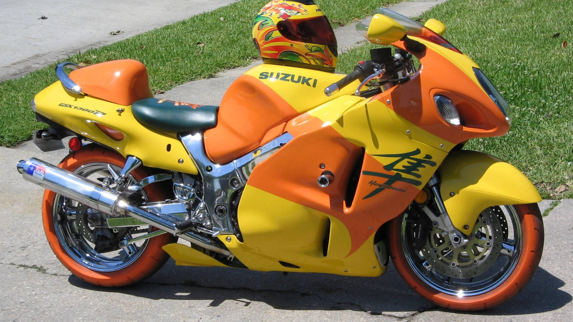 亮色Suzuki Hayabusa 壁紙 — 一輛鮮黃色和橙色的鈴木隼電單車停泊在行人路上，旁邊有綠草，在明亮的陽光下。