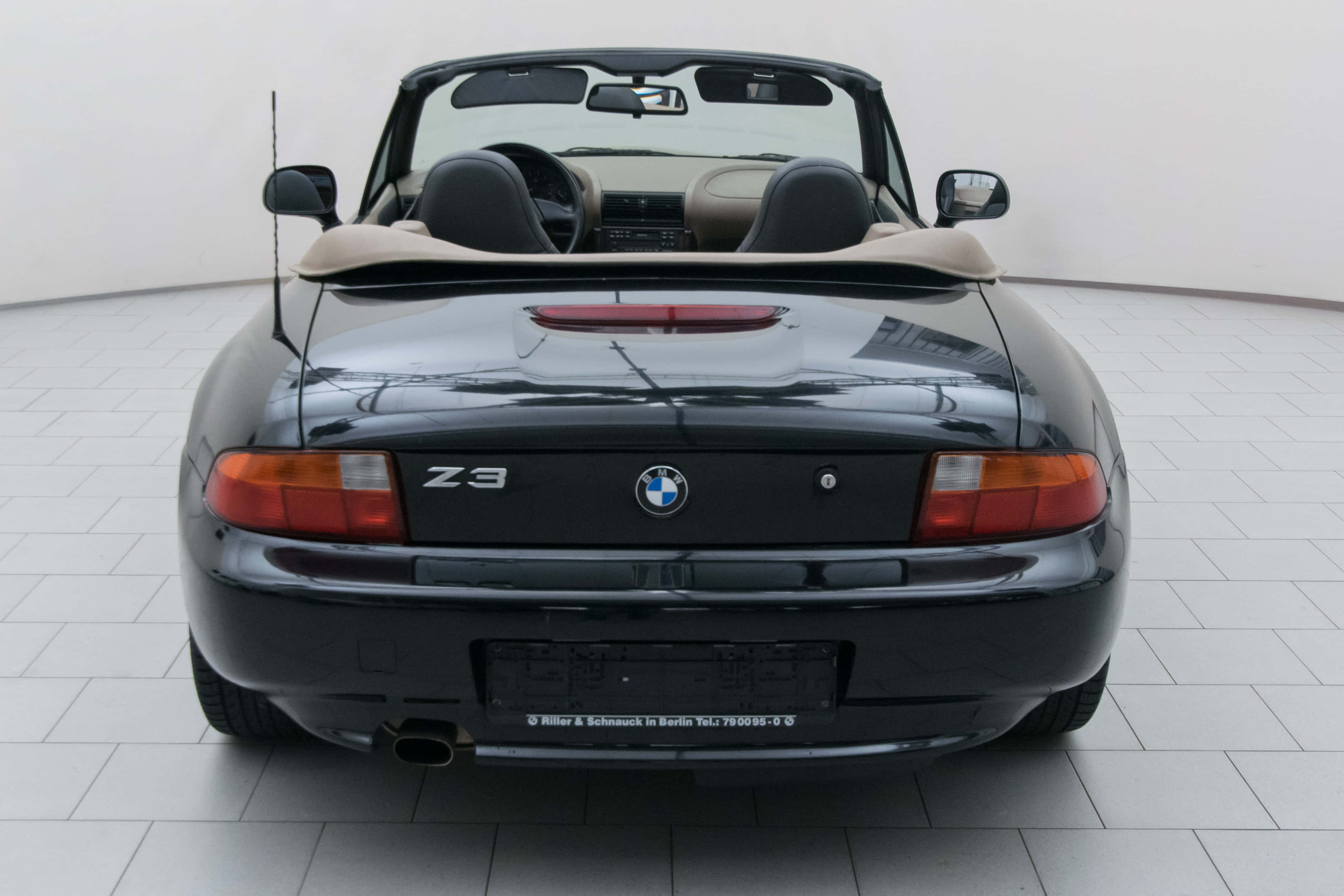 Bmw Z3 桌布 壁紙 — 亮黑色BMW Z3開篷車配米色內飾，停泊在明亮工作室的瓷磚地板上，從後方觀看。