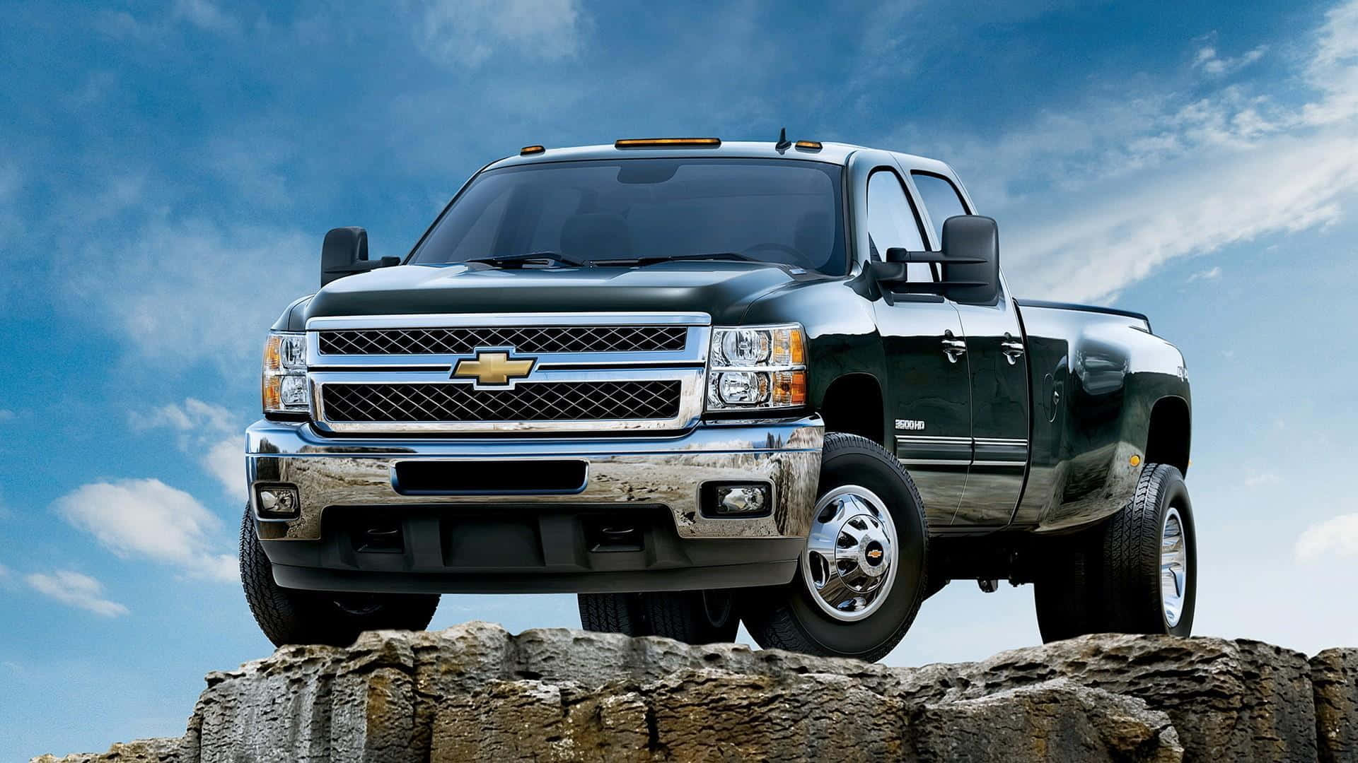 亮黑色雪佛蘭銀河皮卡 壁紙 — 一架深綠色 Chevrolet Silverado  pickup truck 自豪地矗立在崎嶇岩石上，天空湛藍，白雲點綴。