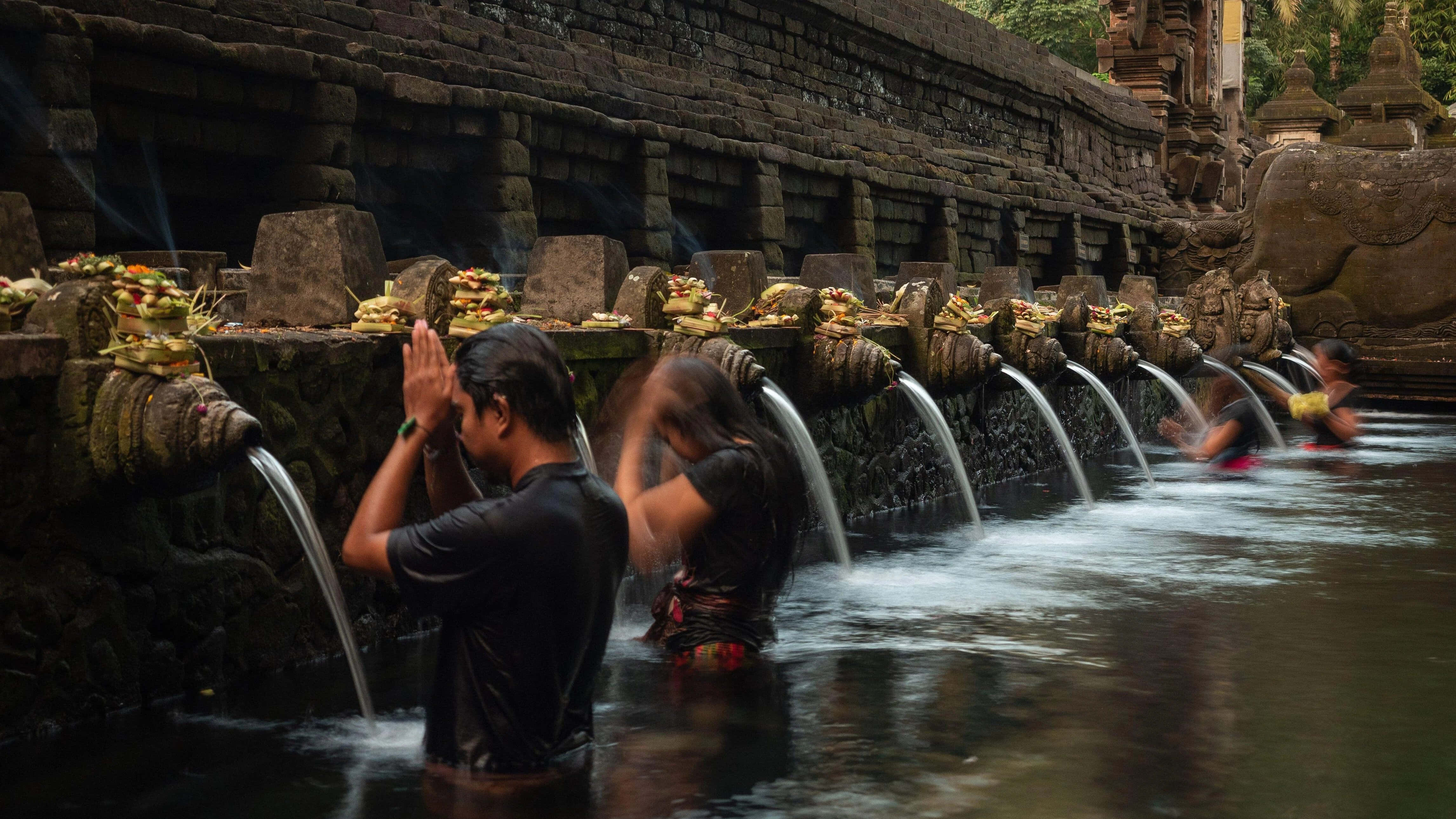 Indonesia 桌布 壁紙 — 人們在峇里島的石廟噴泉中進行神聖儀式，水從雕刻的頭像中傾瀉而下。