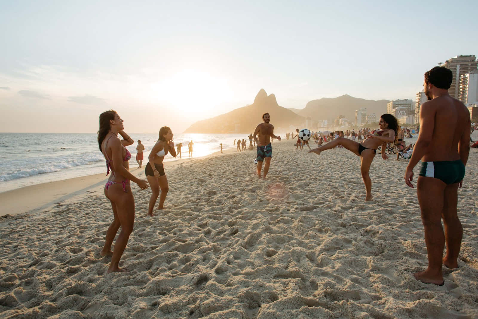Brazilian Beach 桌布 壁紙 — 人們在日落時分踢沙灘足球，背景是糖麵包山。