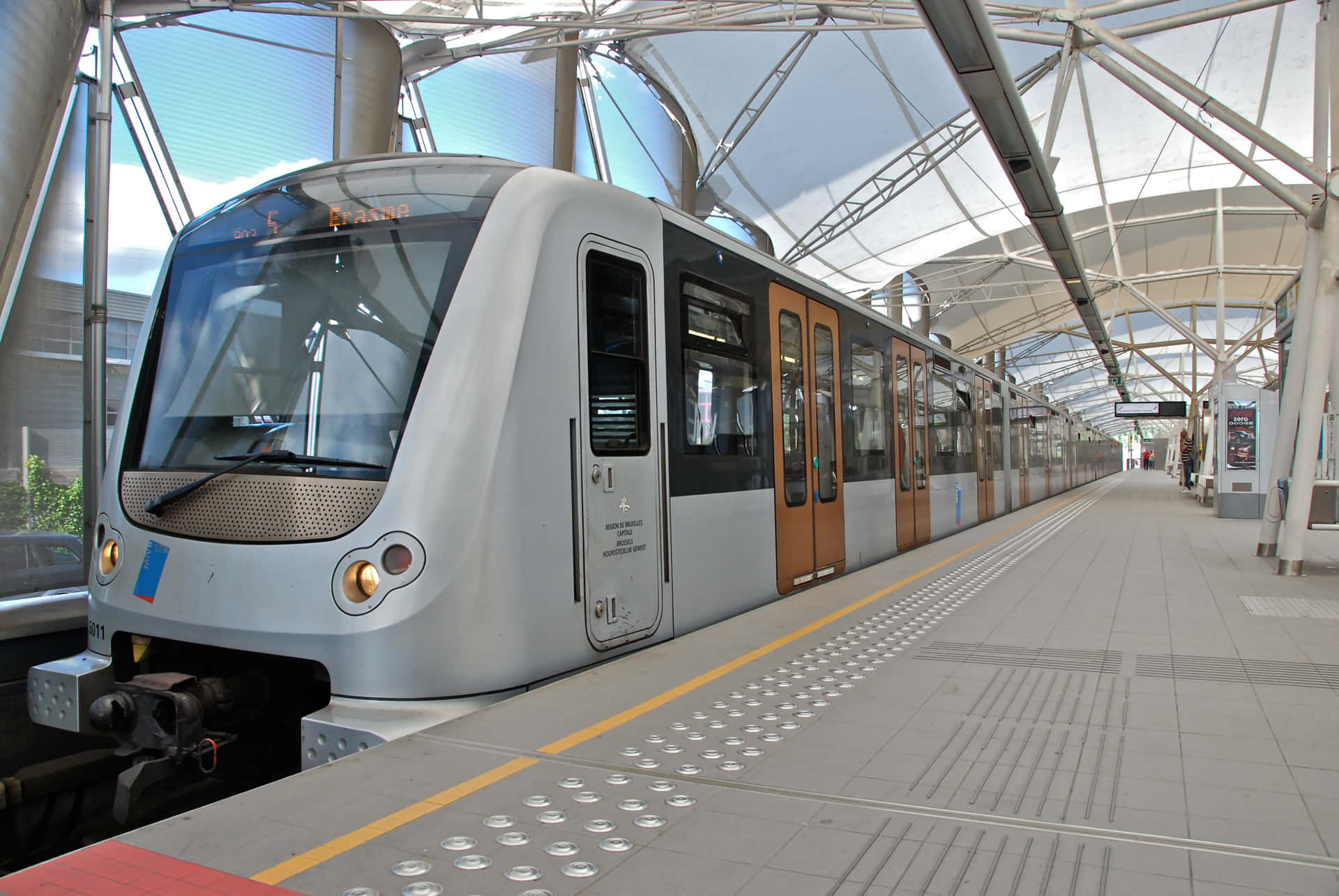 銀色火車在現代化車站月台上，設有玻璃天篷和觸覺引路徑。