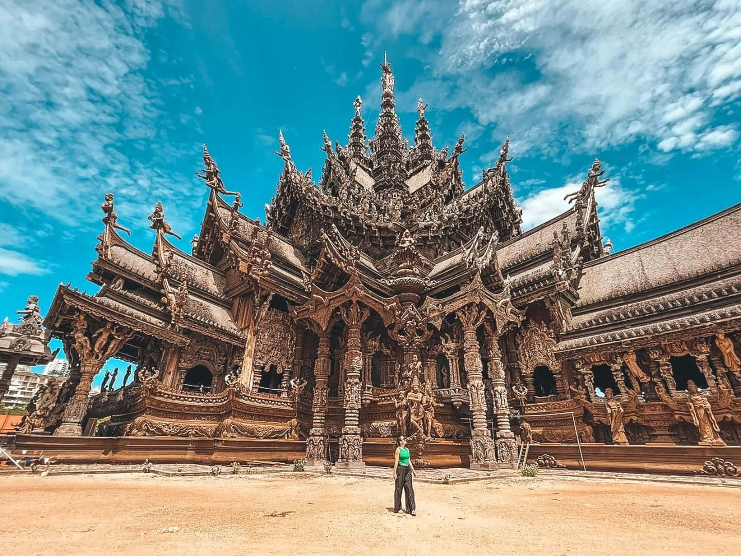 人在巨偉真理聖殿下佇立 壁紙 — 一個人站在精雕細琢的木製白龍寺前，在晴朗藍天和零星白雲下顯得渺小。