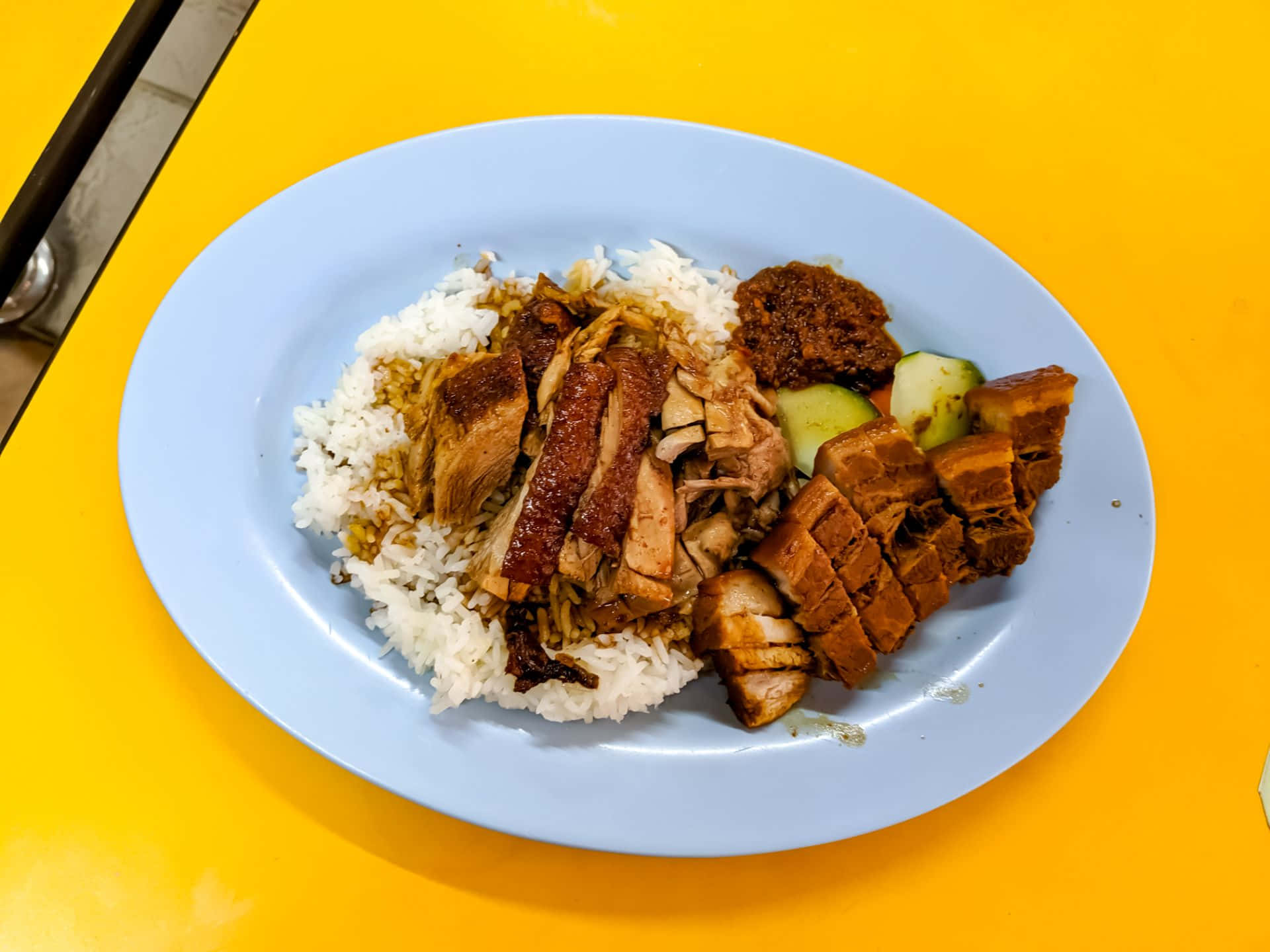 人山人海人民公園的立記正宗潮州滷鴨飯 壁紙 — 一盤多汁的烤肉和米飯放在一張充滿活力的黃色桌子上，飾以青瓜和辣醬。