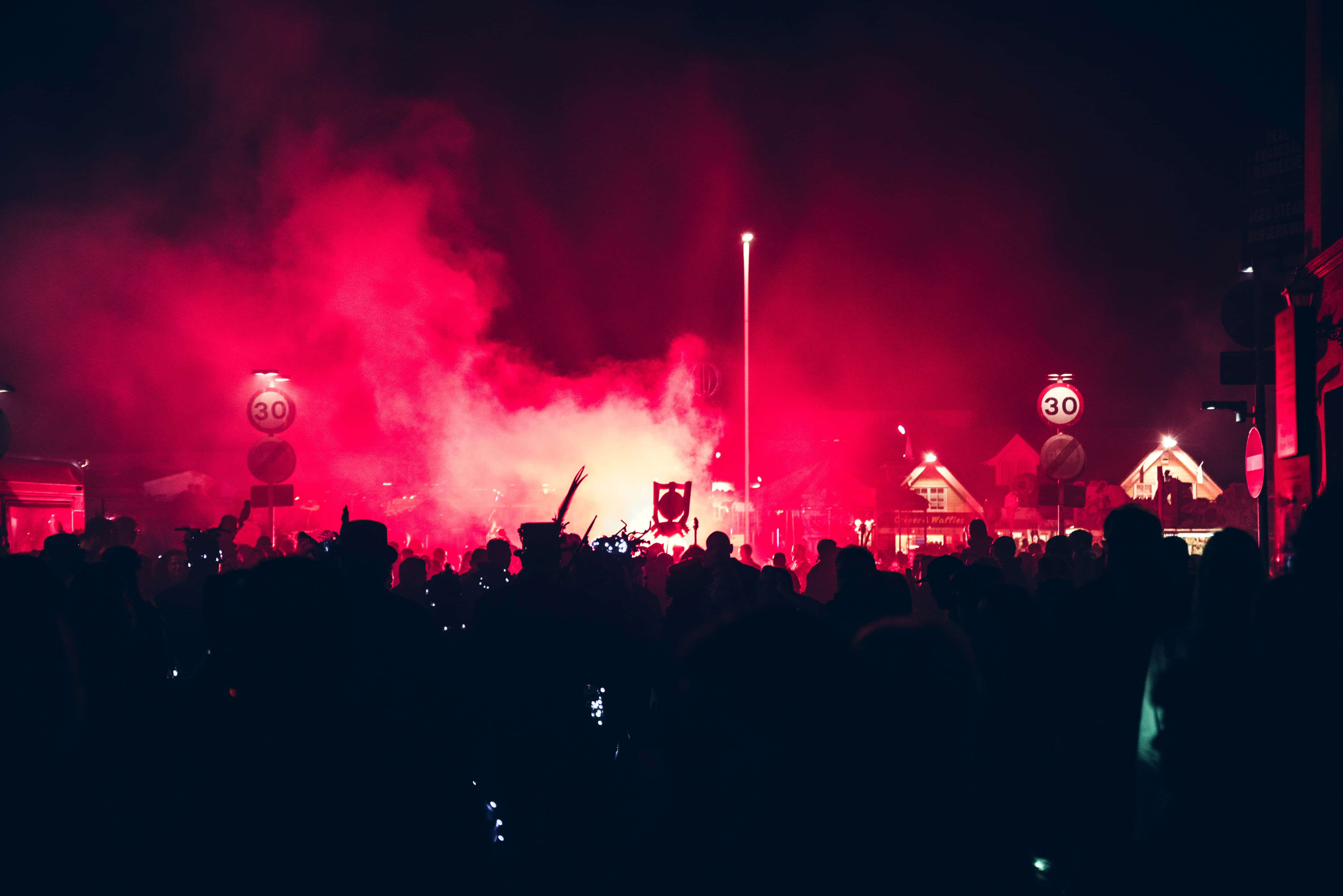 music festival 桌布 壁紙 — 人群在充滿活力紅煙的夜間場景中形成剪影，伴隨著發光的街道標誌和遠處的建築物。