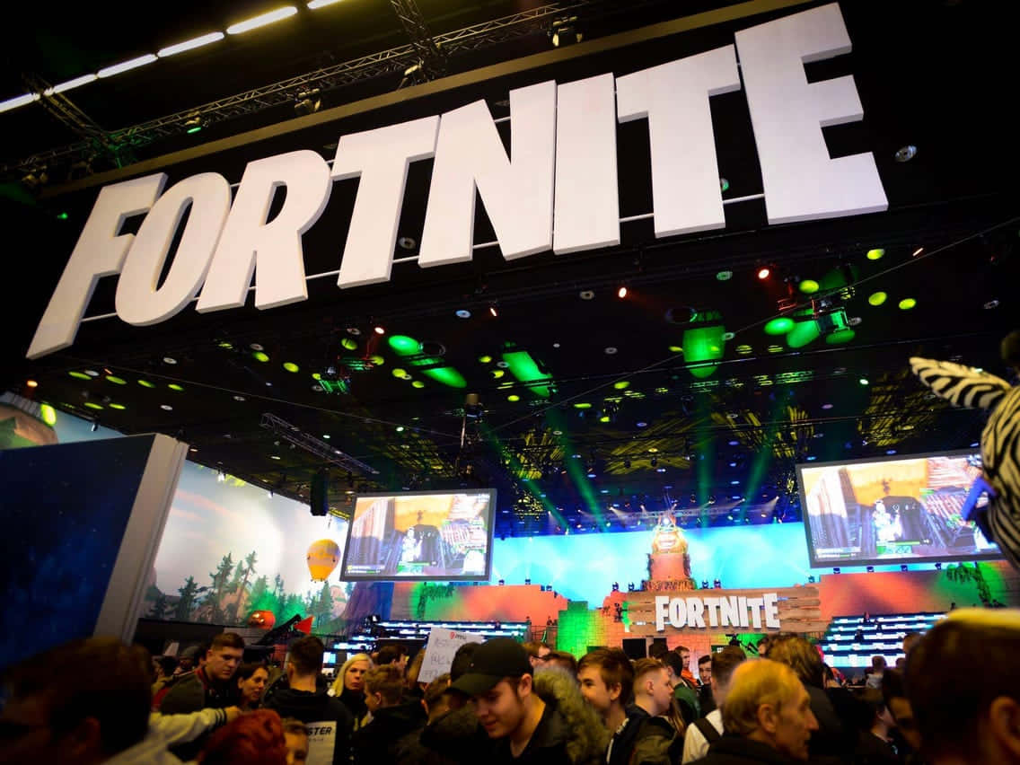 Gaming Conventions 桌布 壁紙 — 人群聚集在一個巨大的Fortnite標誌下，參加一場充滿活力的遊戲展會，現場有發光的綠色燈光和大螢幕。