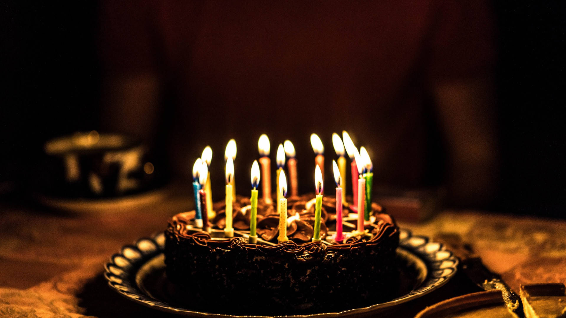今天是我的生日圓形蛋糕 壁紙 — 在昏暗的房間裡，一個朱古力生日蛋糕上插著色彩繽紛的點燃蠟燭，溫暖地閃耀著。