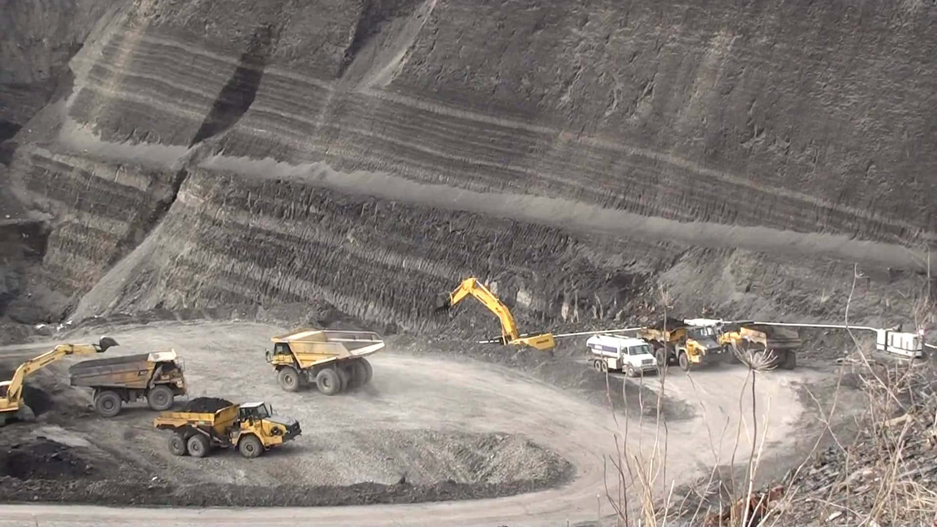 今日辛勤工作的煤礦工人 壁紙 — 巨大的黃色自卸卡車和挖掘機在一個擁有梯田狀岩壁的廣闊露天礦場中作業。
