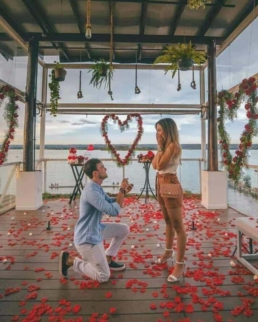 男人在鋪滿玫瑰花瓣的甲板上，以心形裝飾和湖景為背景向女人求婚。