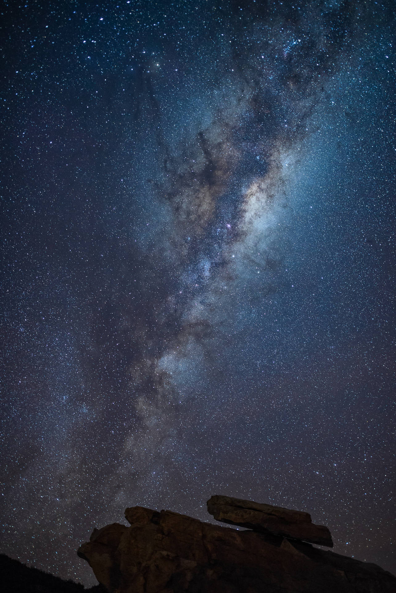 在繁星點點的夜空下，銀河系在黑色岩石剪影上方閃耀